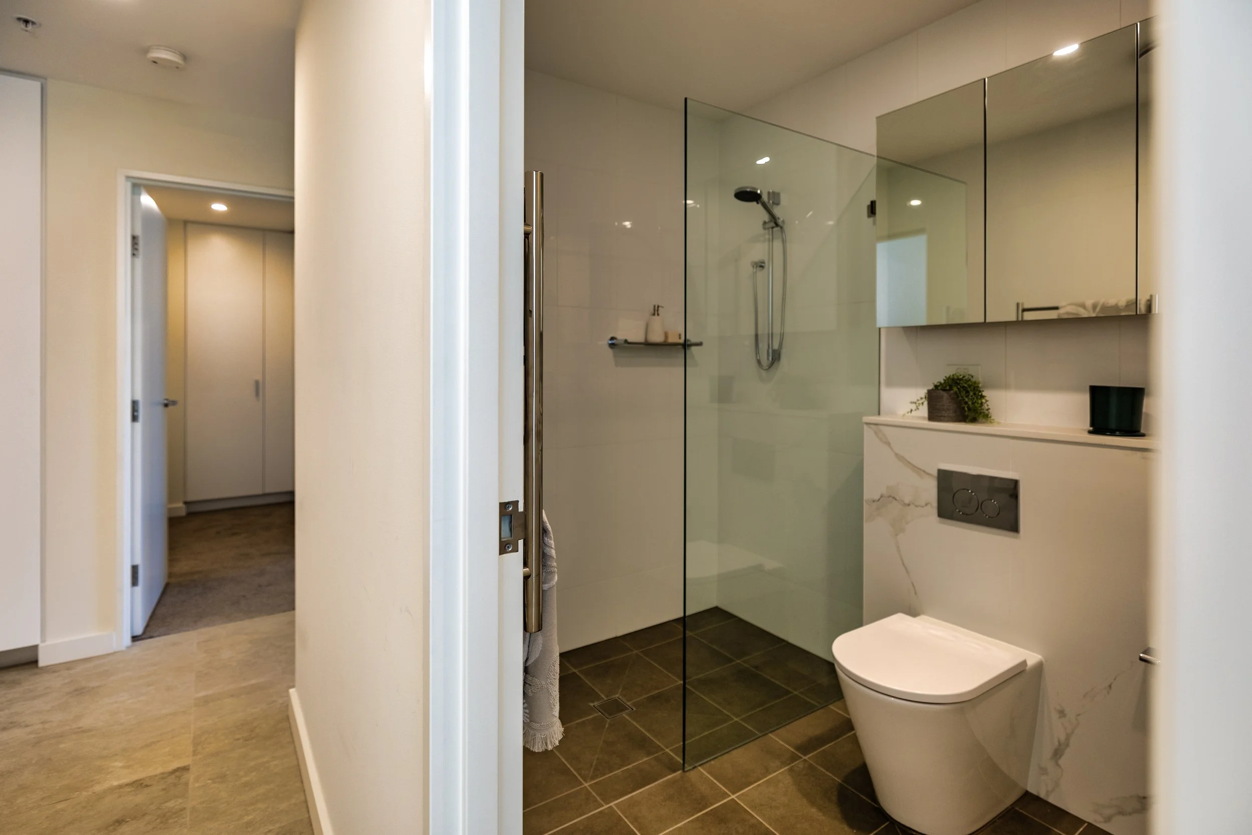 Modern bathroom with a glass shower enclosure, white toilet, wall-mounted storage, and minimal decor.