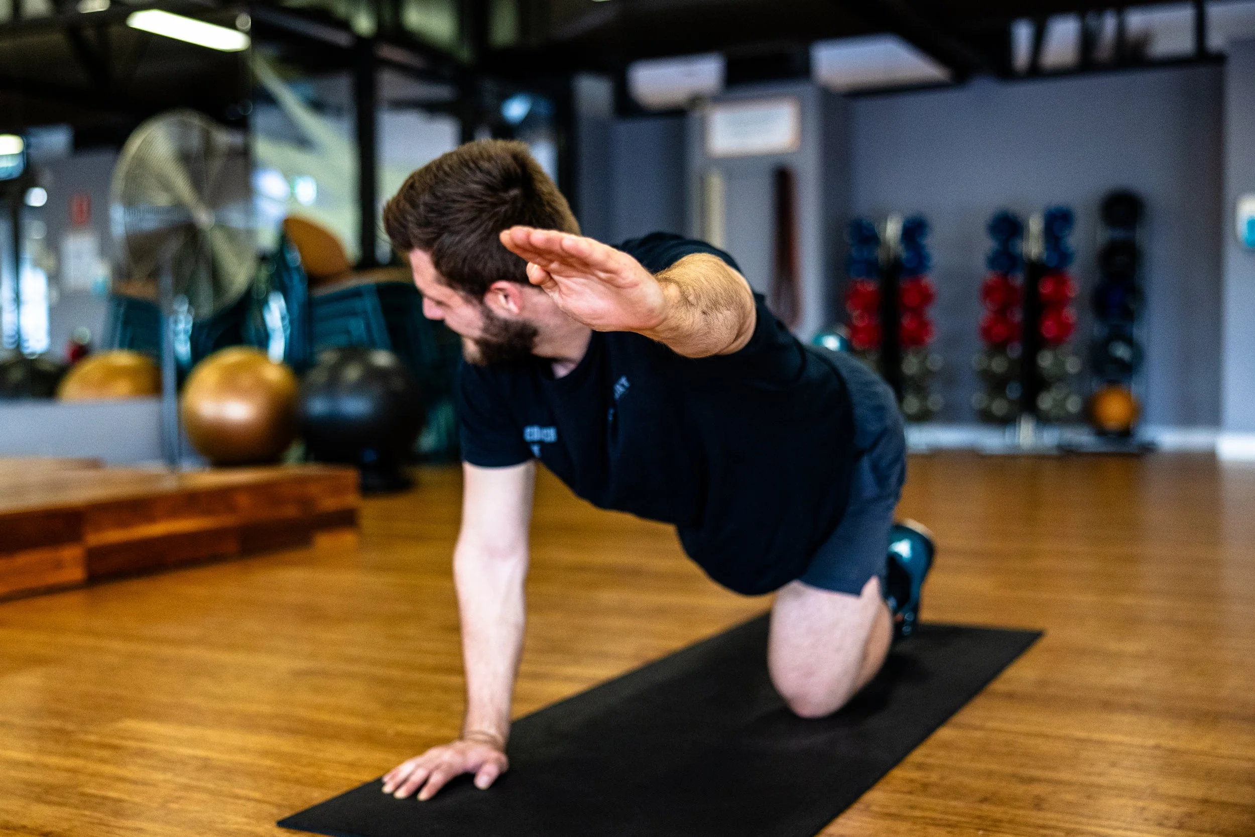 Man performing a yoga pose on a black mat in a gym.