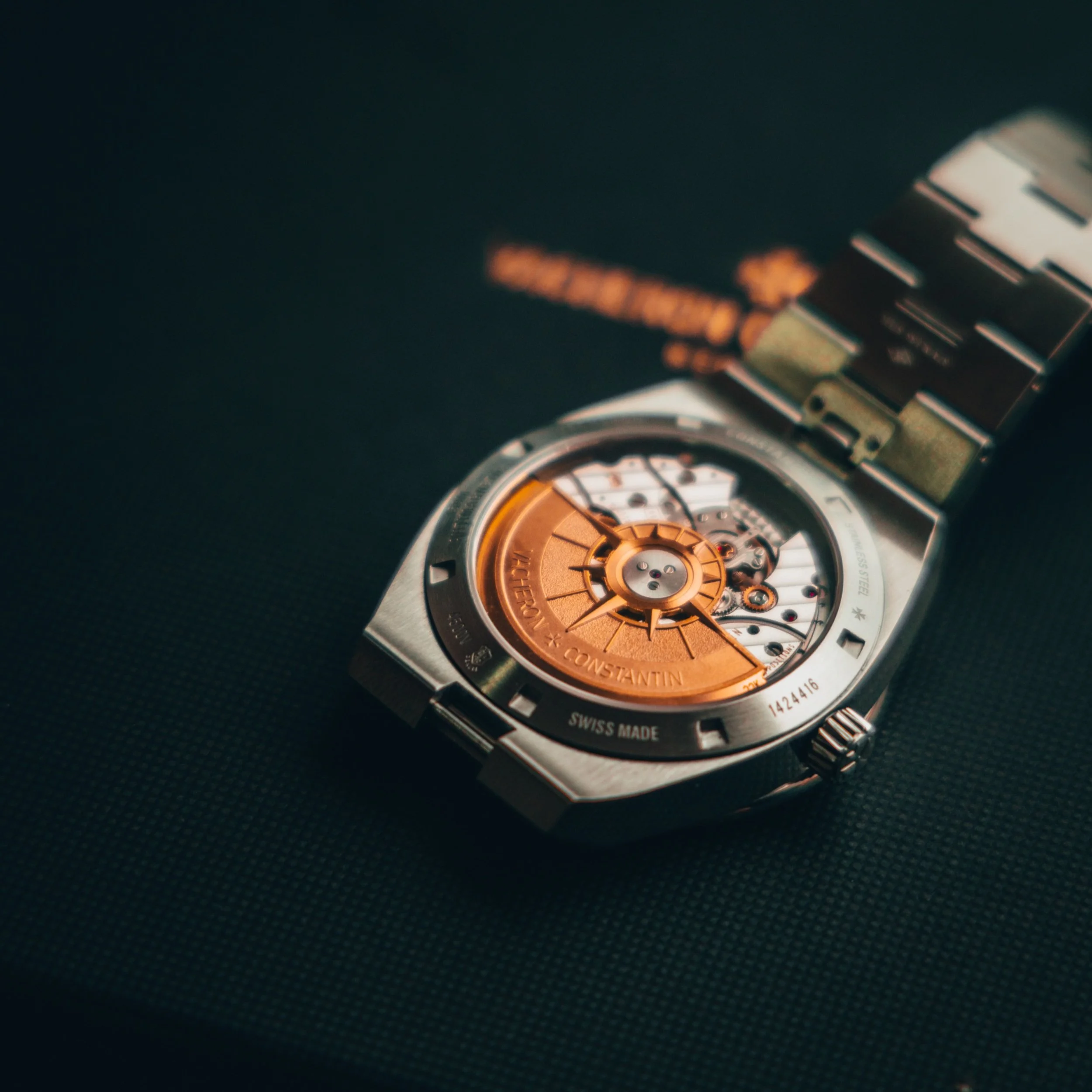 A luxury Swiss-made wristwatch with an open skeleton dial, displaying its intricate mechanical movement, gold rotor, and metallic strap, on a dark surface.