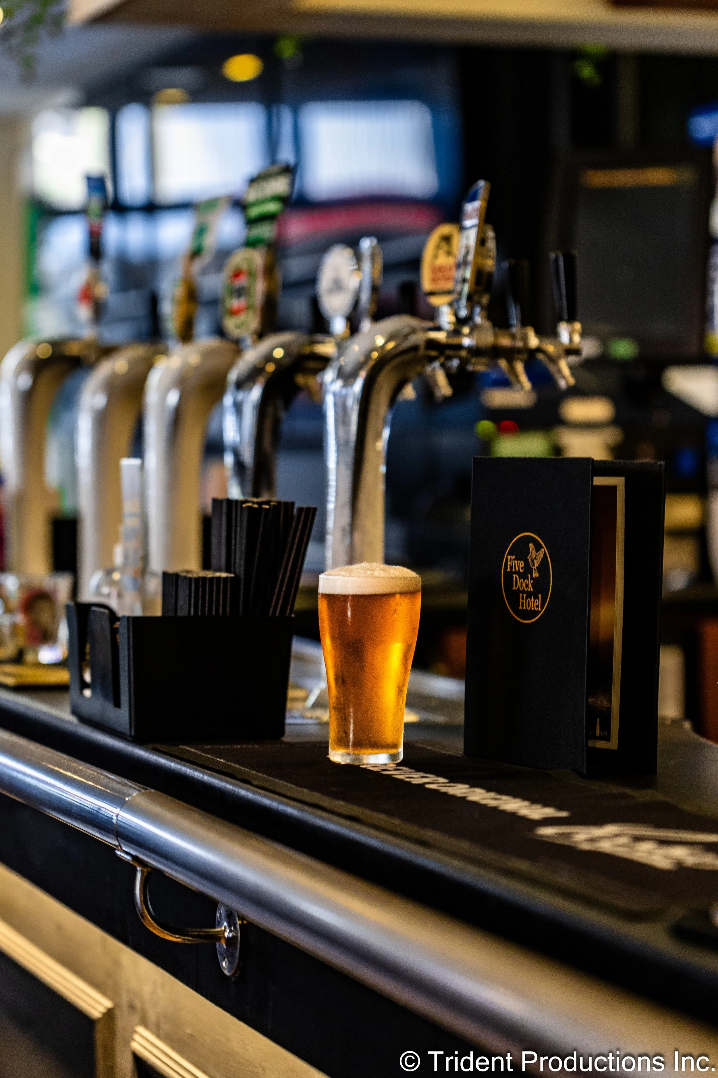A glass of beer placed on a bar counter with beer taps in the background.