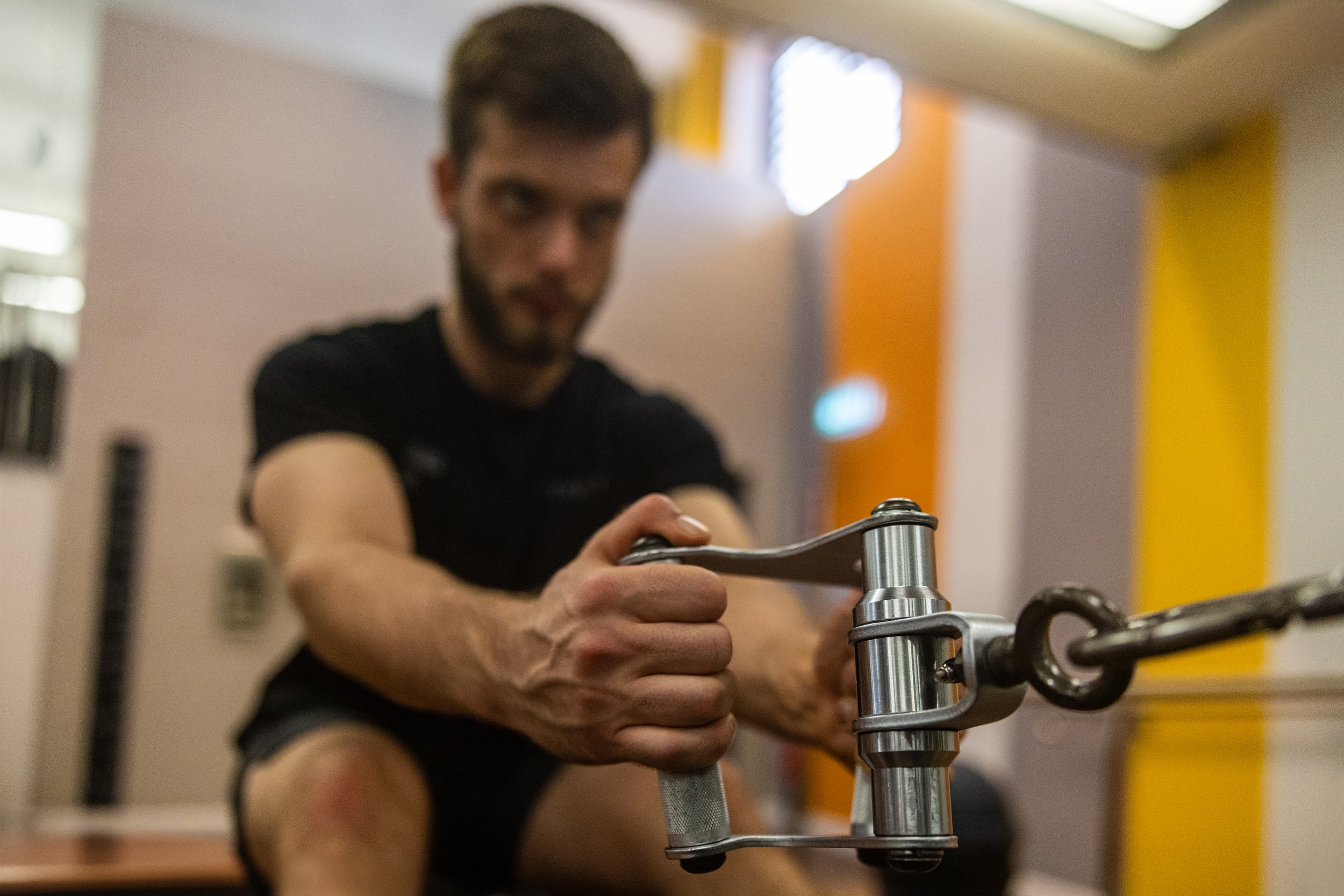 A man using a rowing machine at the gym, focusing on his hand gripping the handle.