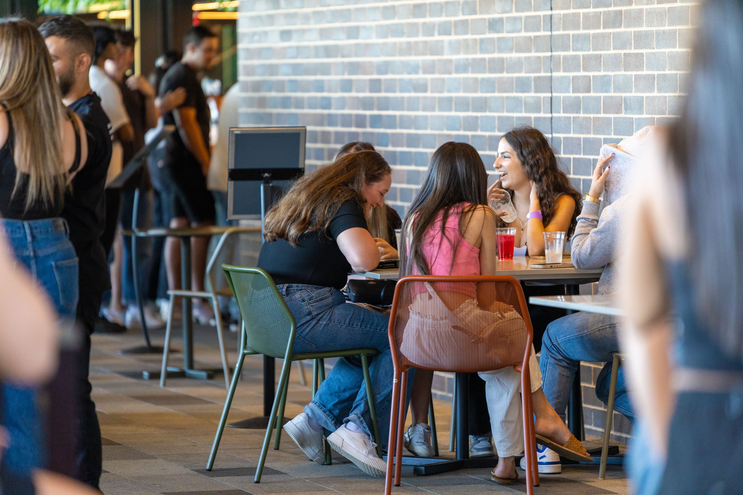 Group of young women sitting at a table in a cafe or restaurant, engaged in conversation and laughing.