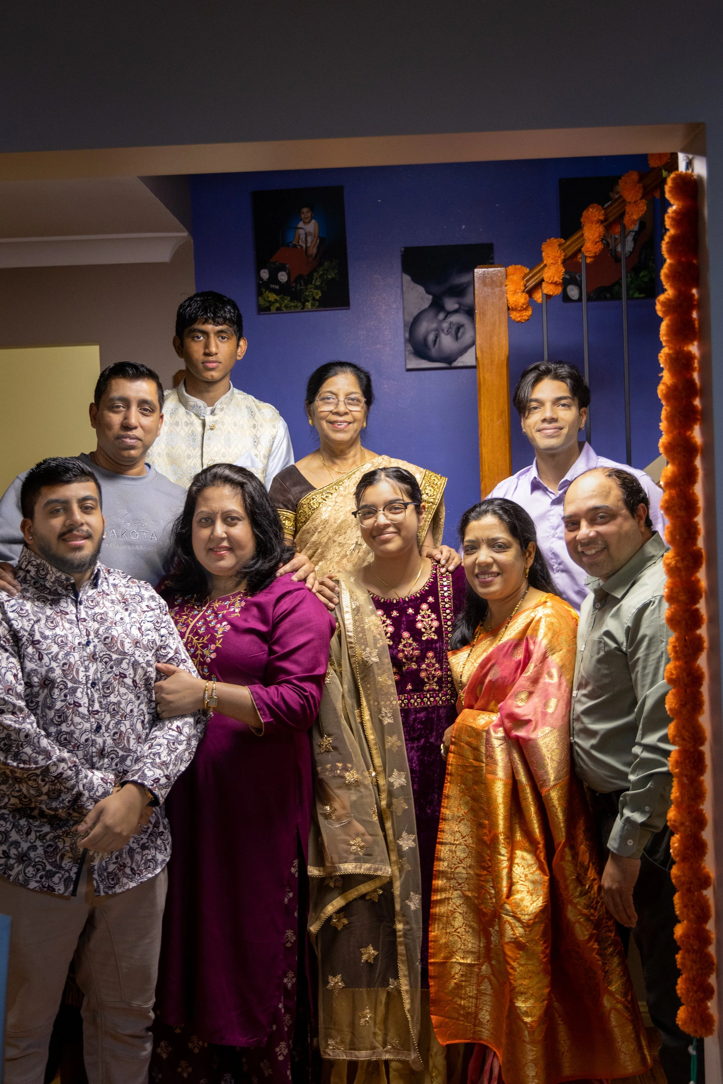 A group of ten South Asian people, including men and women, are gathered together indoors, celebrating a special occasion, with some dressed in traditional Indian attire.