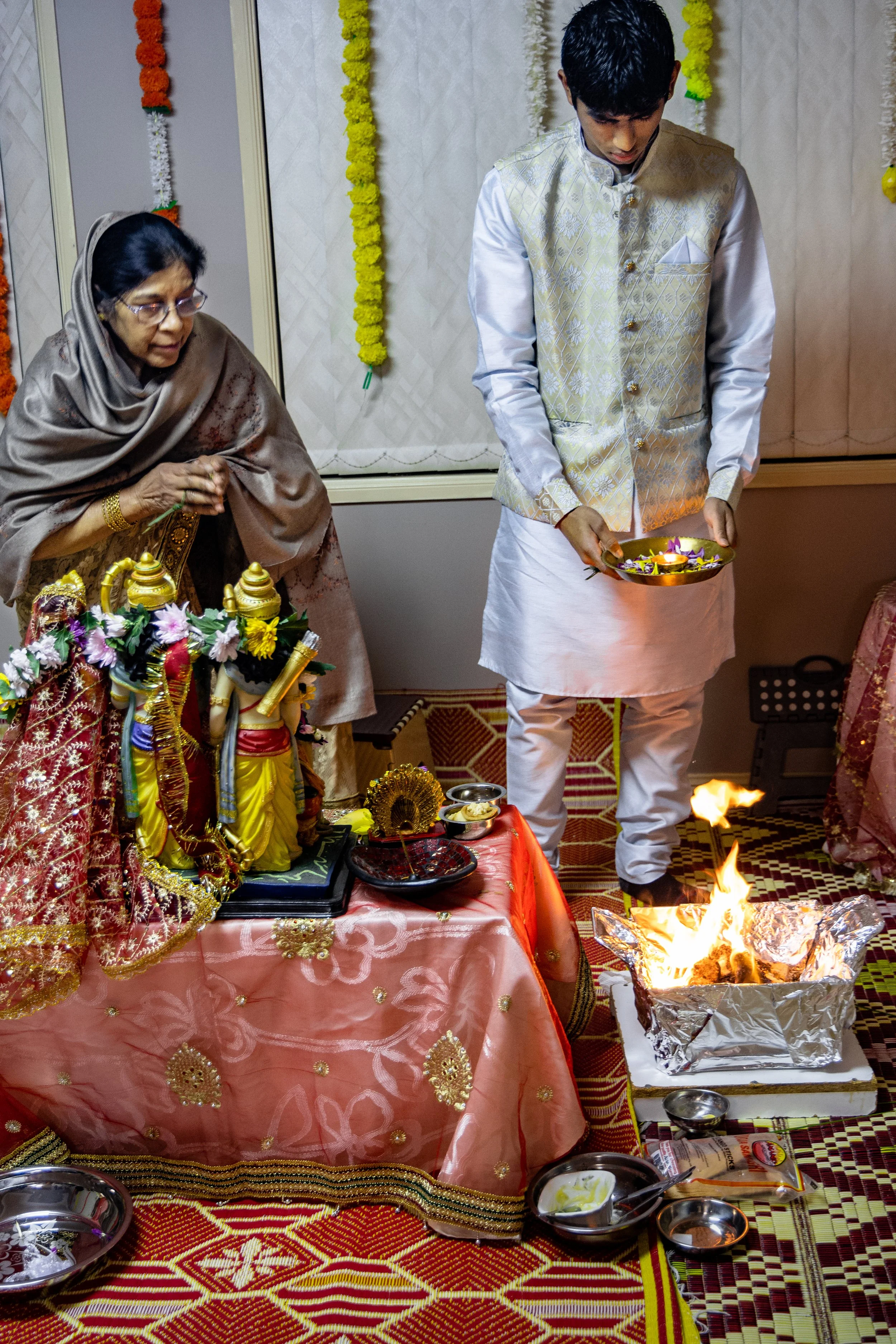 Indian man and woman performing a religious ceremony with statues, offerings, and a fire on a decorated table.