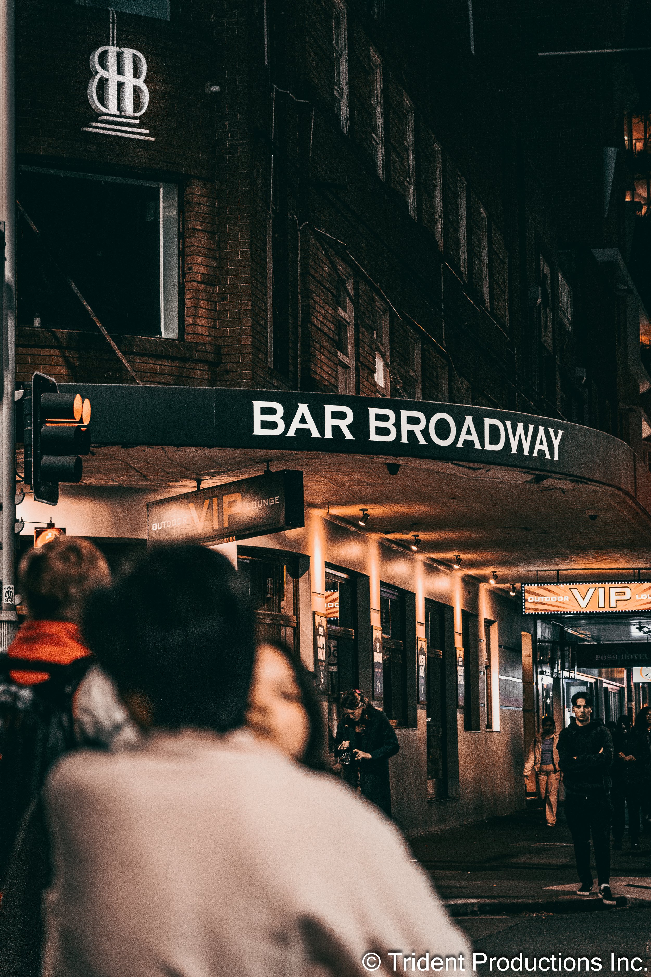 Nighttime street scene outside Bar Broadway with people walking and the VIP lounge sign visible.
