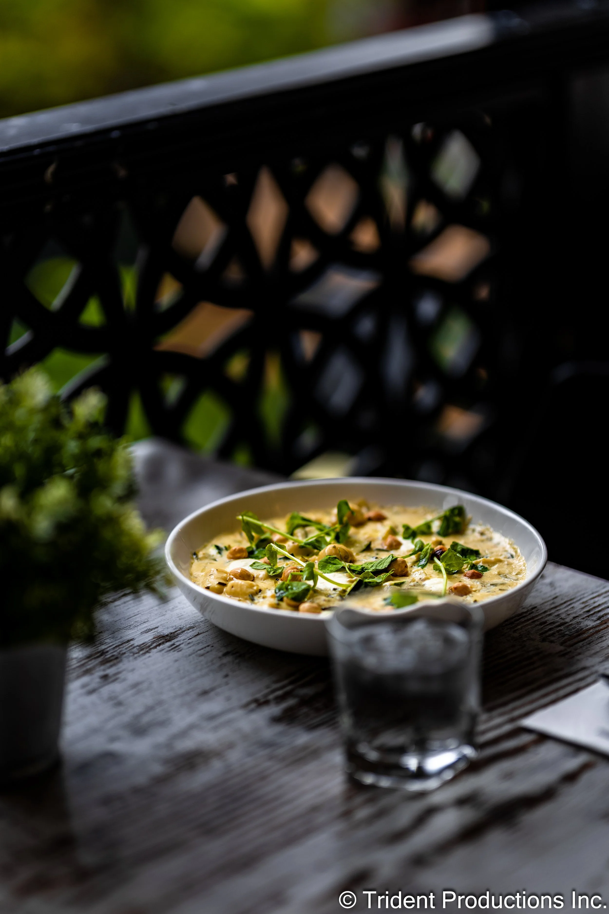 A bowl of creamy soup topped with green herbs and chickpeas, placed on a rustic wooden table outdoors.