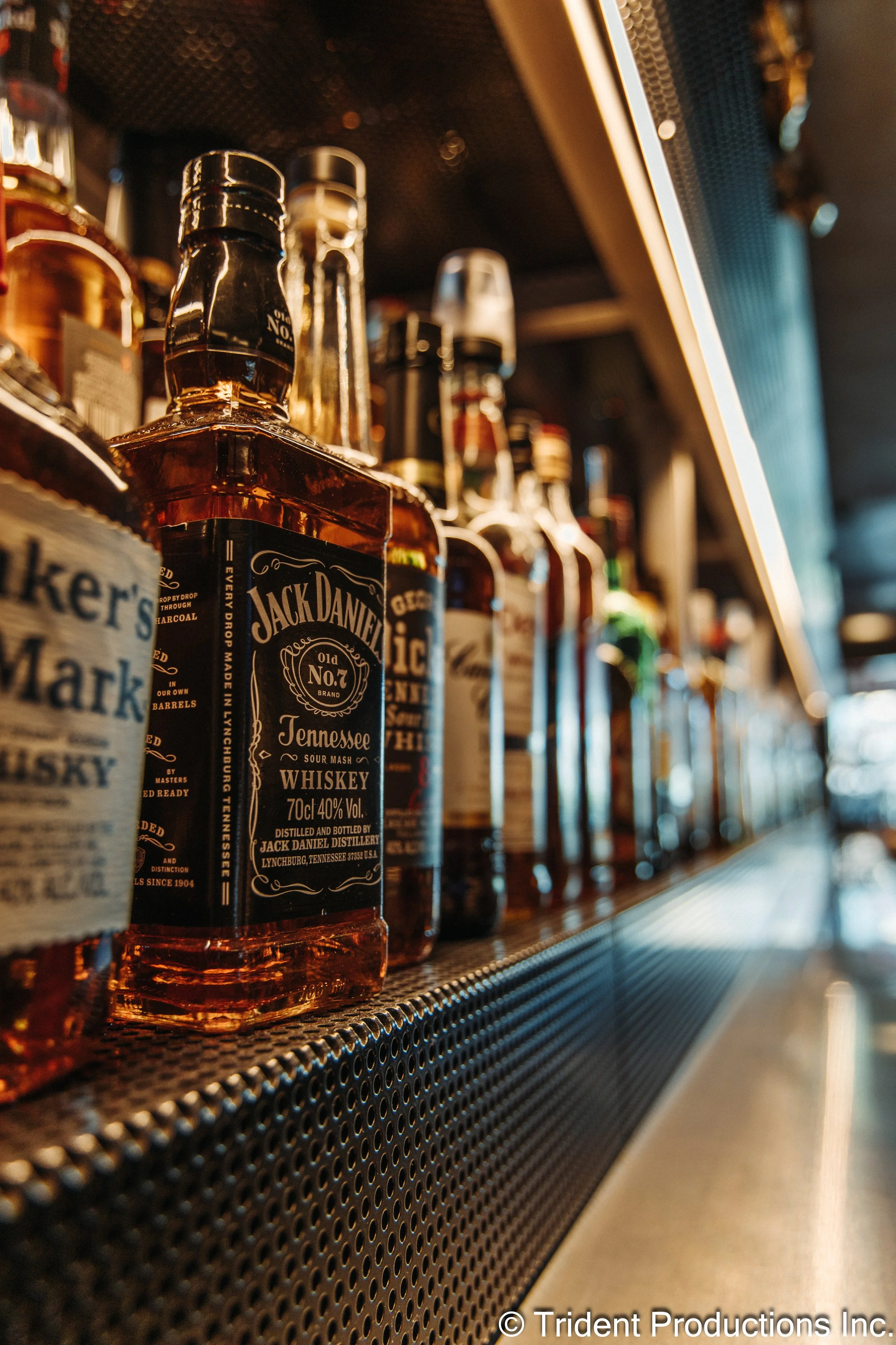 Close-up of various bottles of whiskey on a bar counter, with a focus on a Jack Daniel's whiskey bottle, in a bar setting.