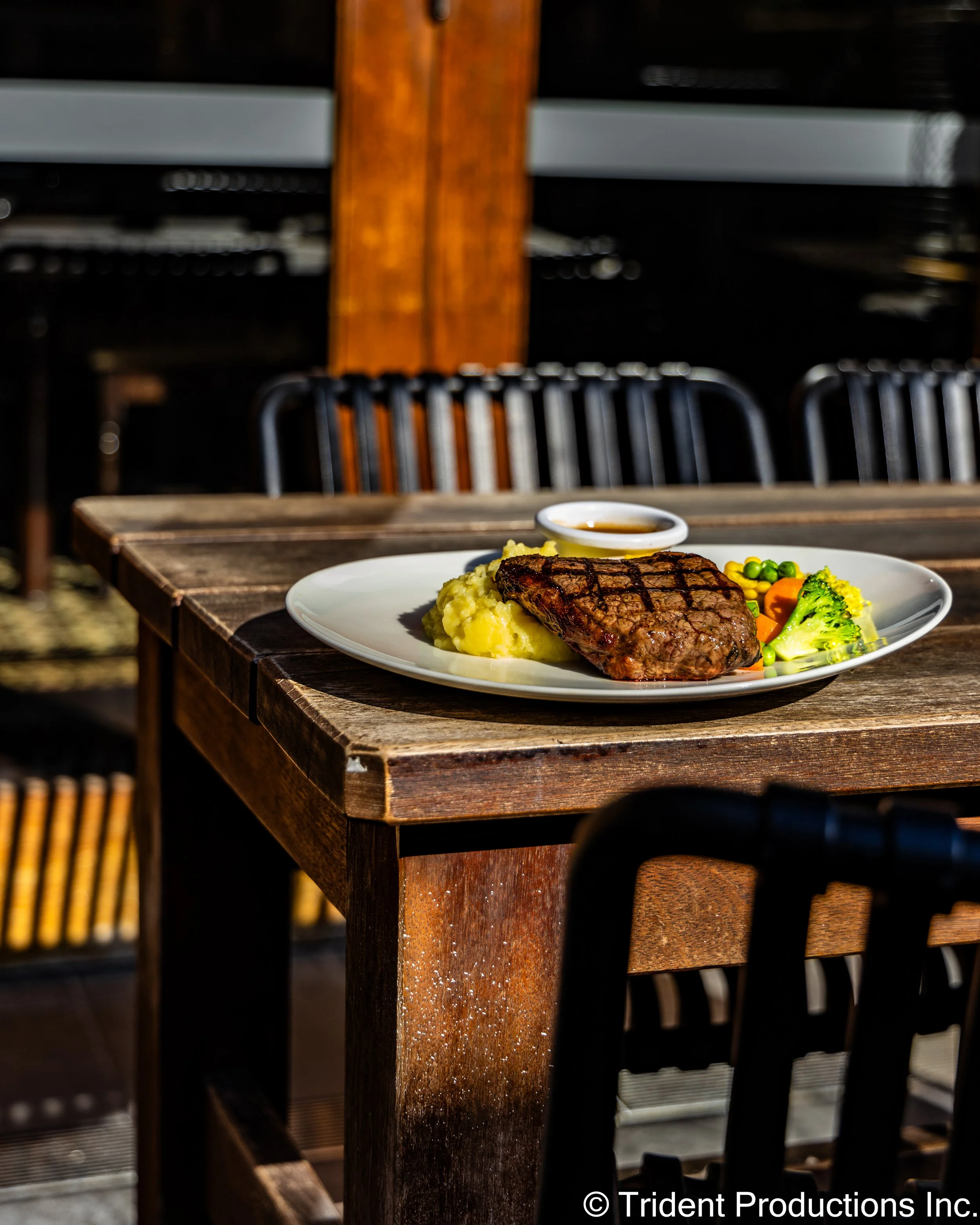 A plate of grilled steak with mashed potatoes, vegetables, and dipping sauce on a rustic wooden table.