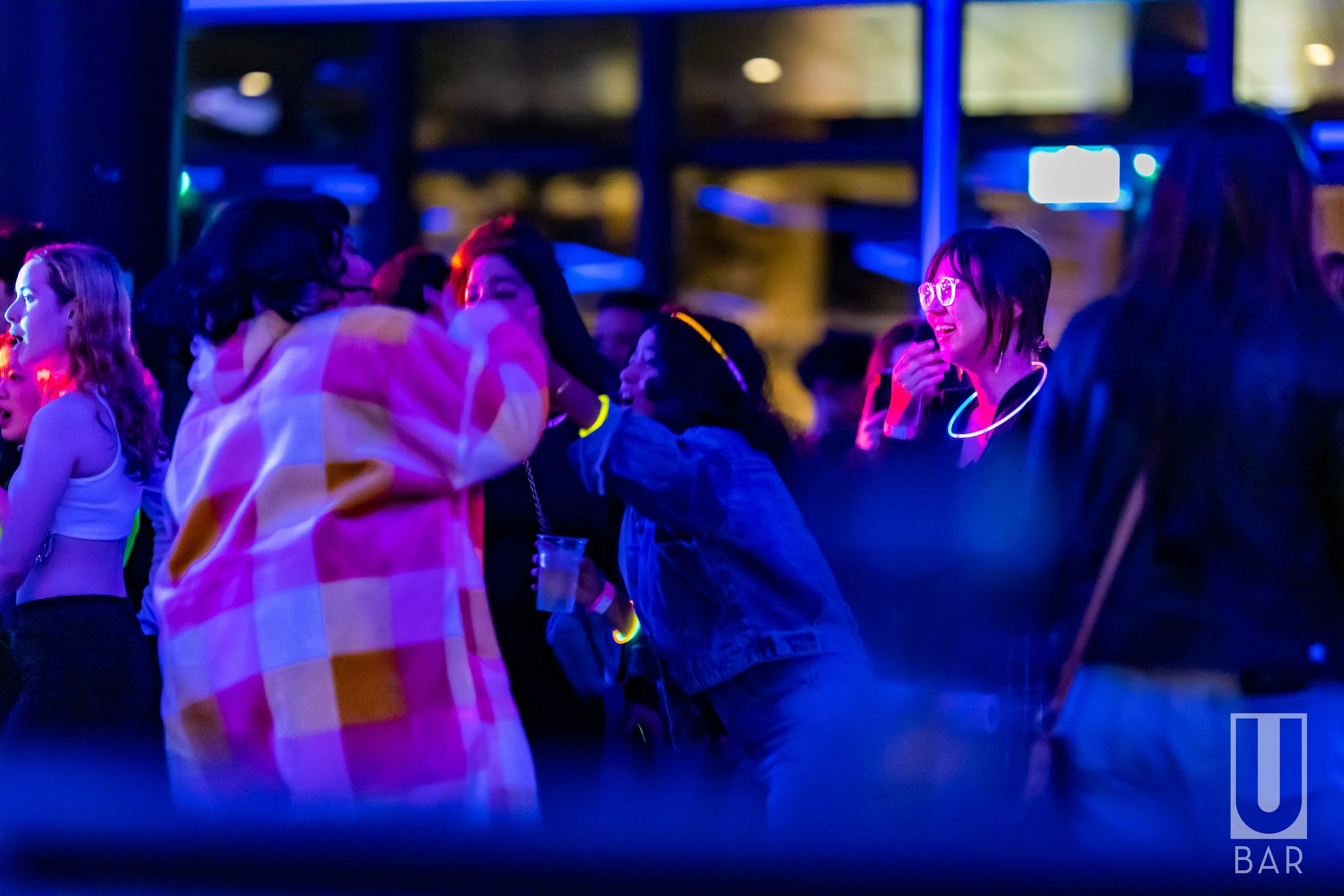 People dancing and socializing at a nightclub with colorful neon lighting.
