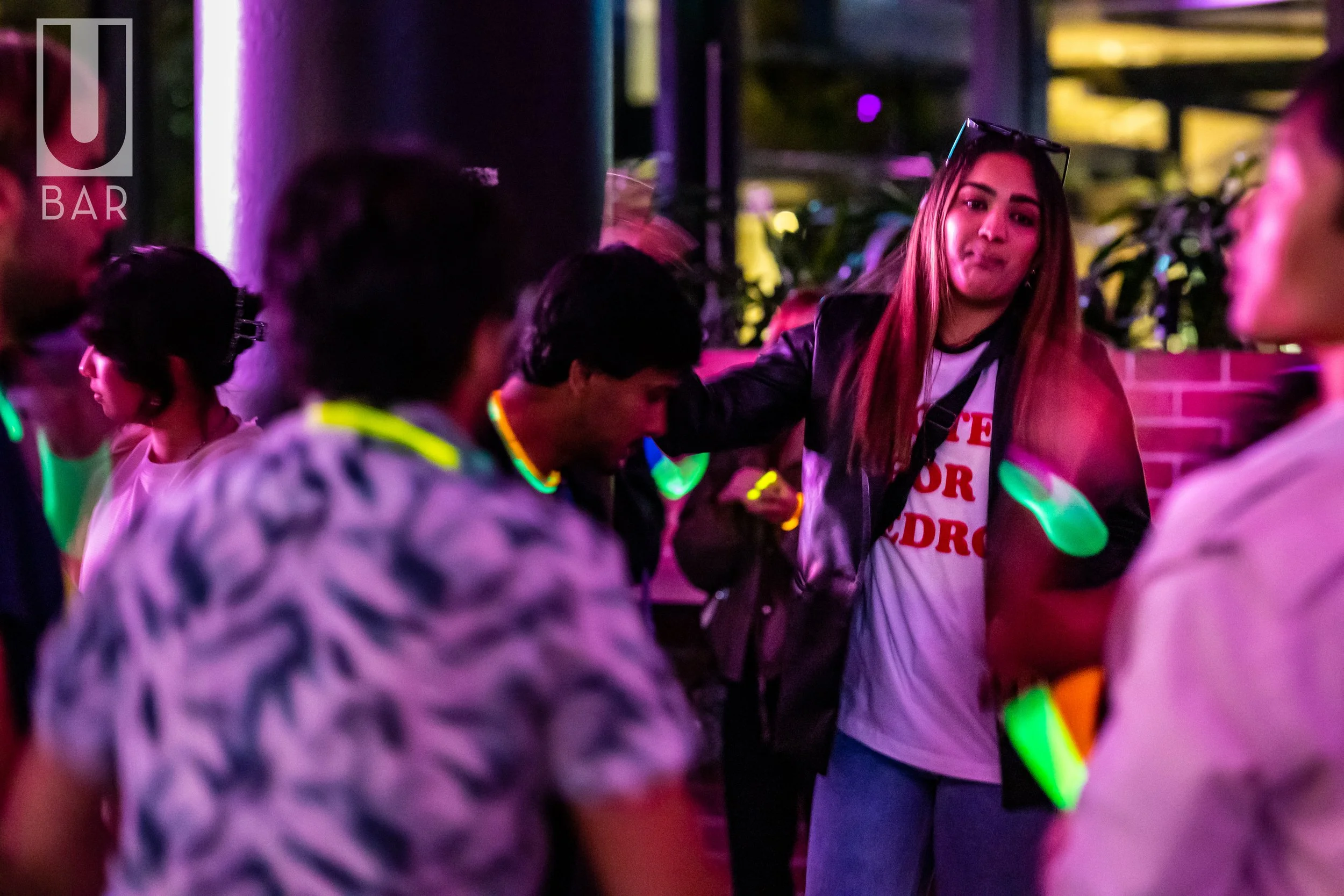 People dancing at a party or nightclub with colorful lights and glow accessories.