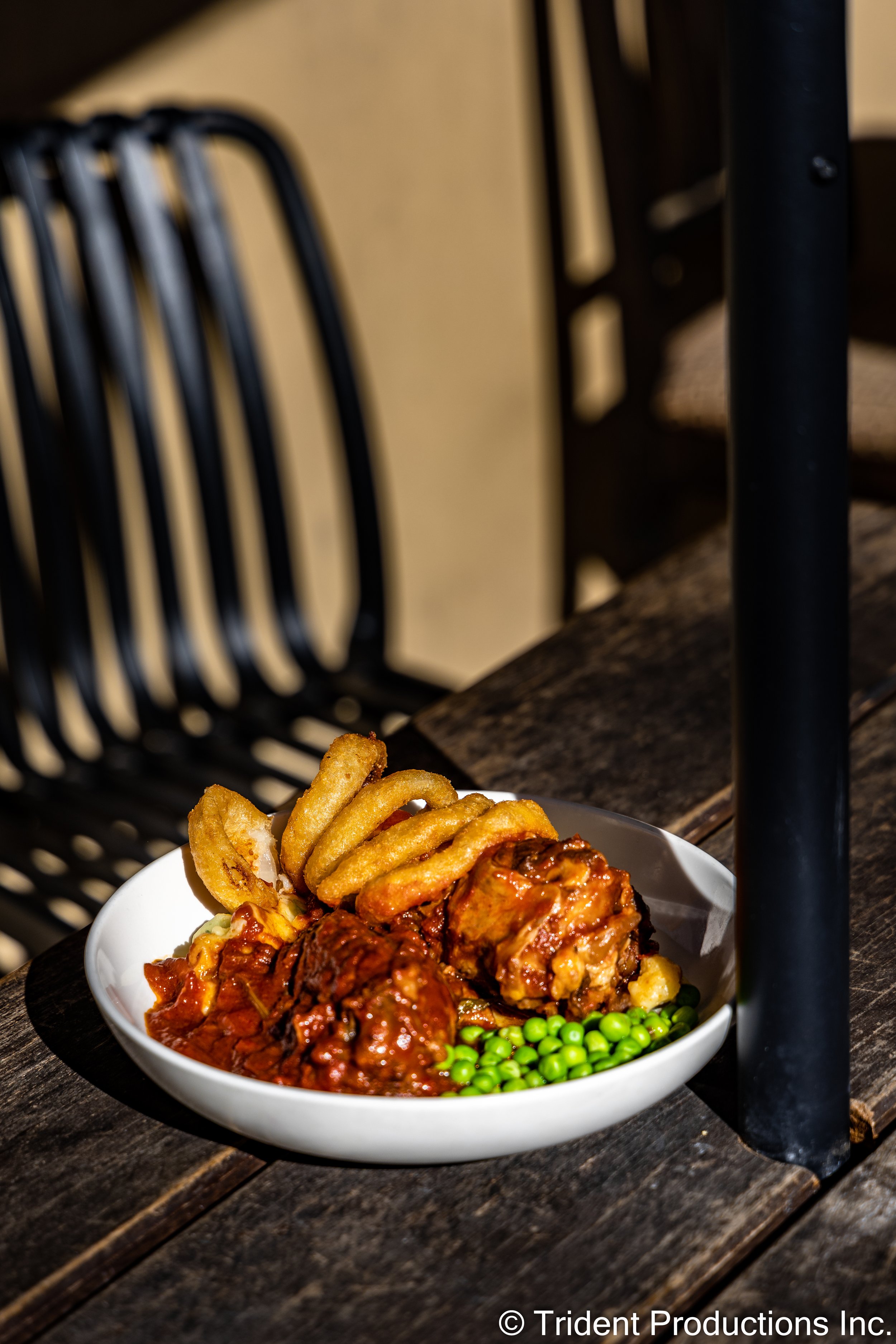 A white bowl of meatloaf with onion rings, green peas, and tomato sauce on a rustic wooden table.