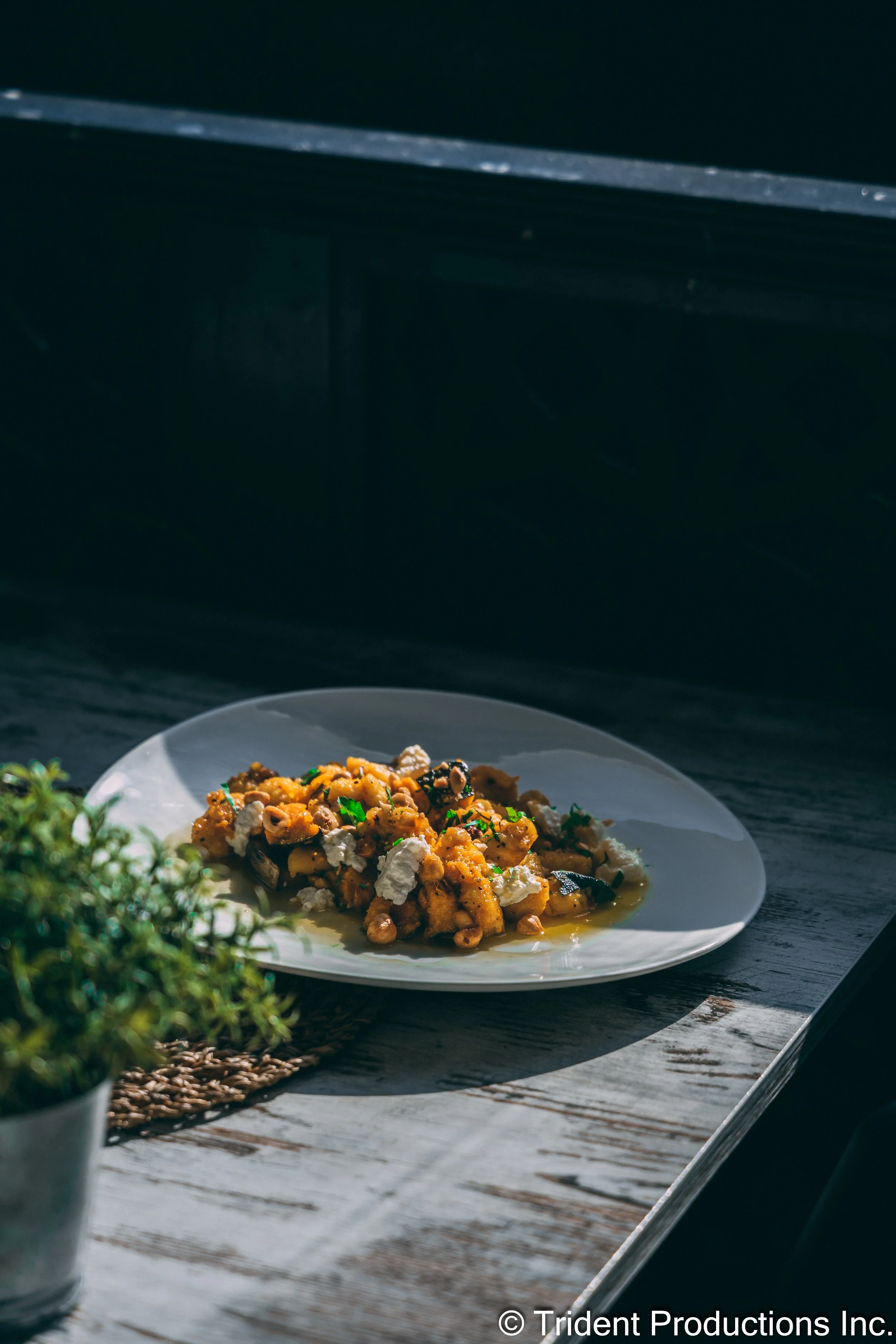 Plate of cooked food with vegetables and toppings on a rustic wooden table with natural sunlight.