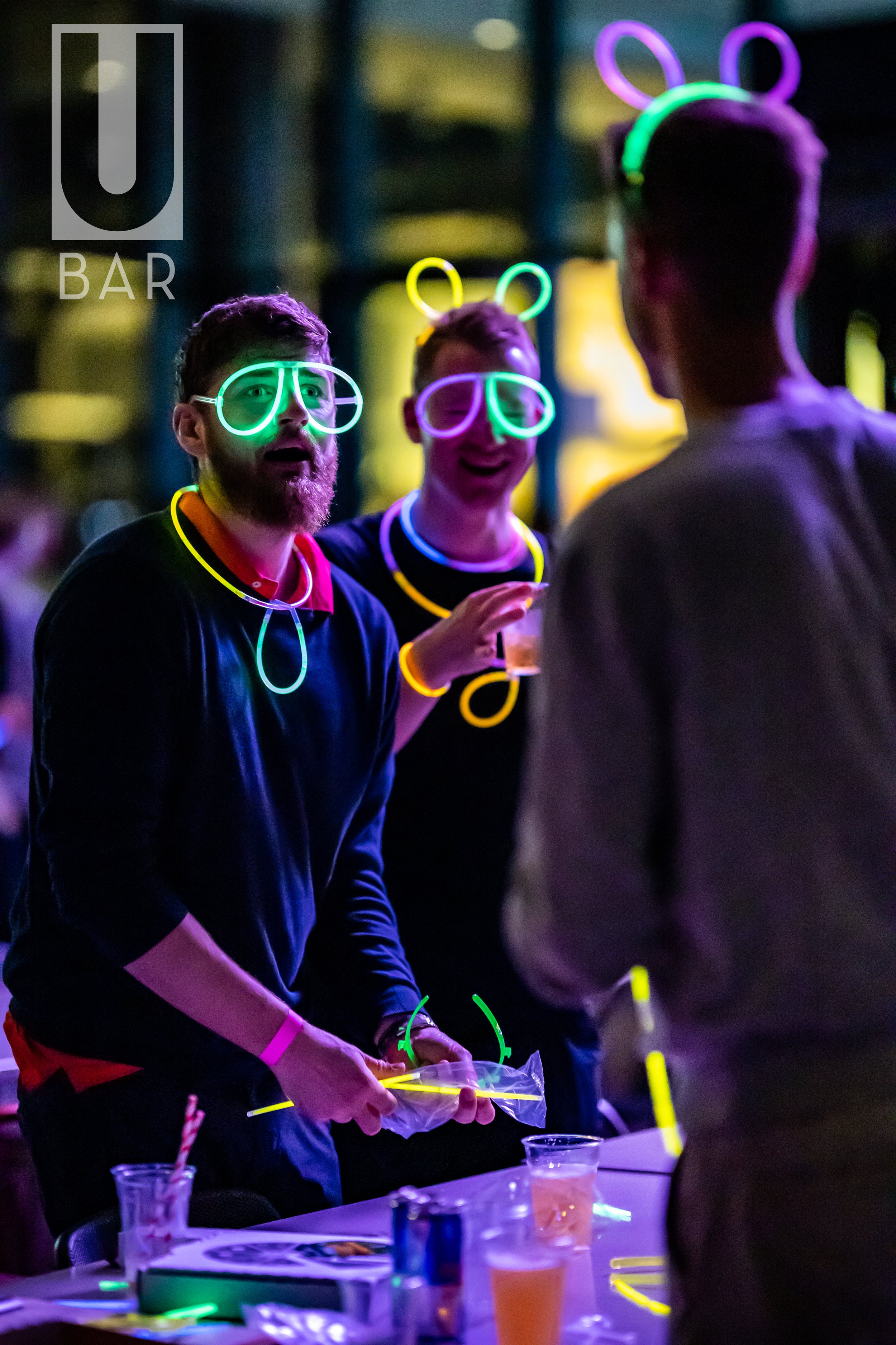People wearing neon glow accessories and glasses at a bar during a party.