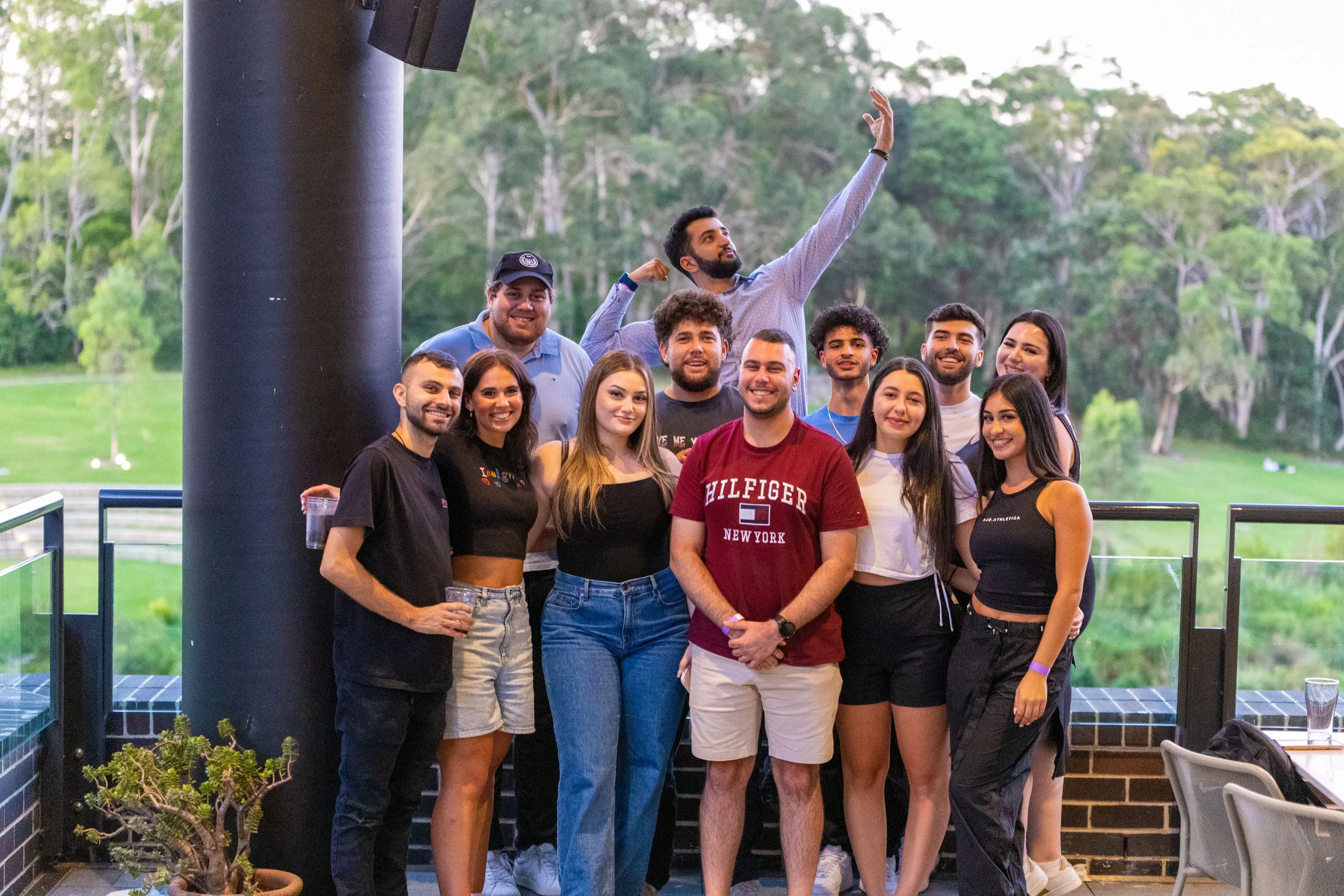 Group of people smiling and posing for a photo outdoors, with trees and grass in the background, during daytime.