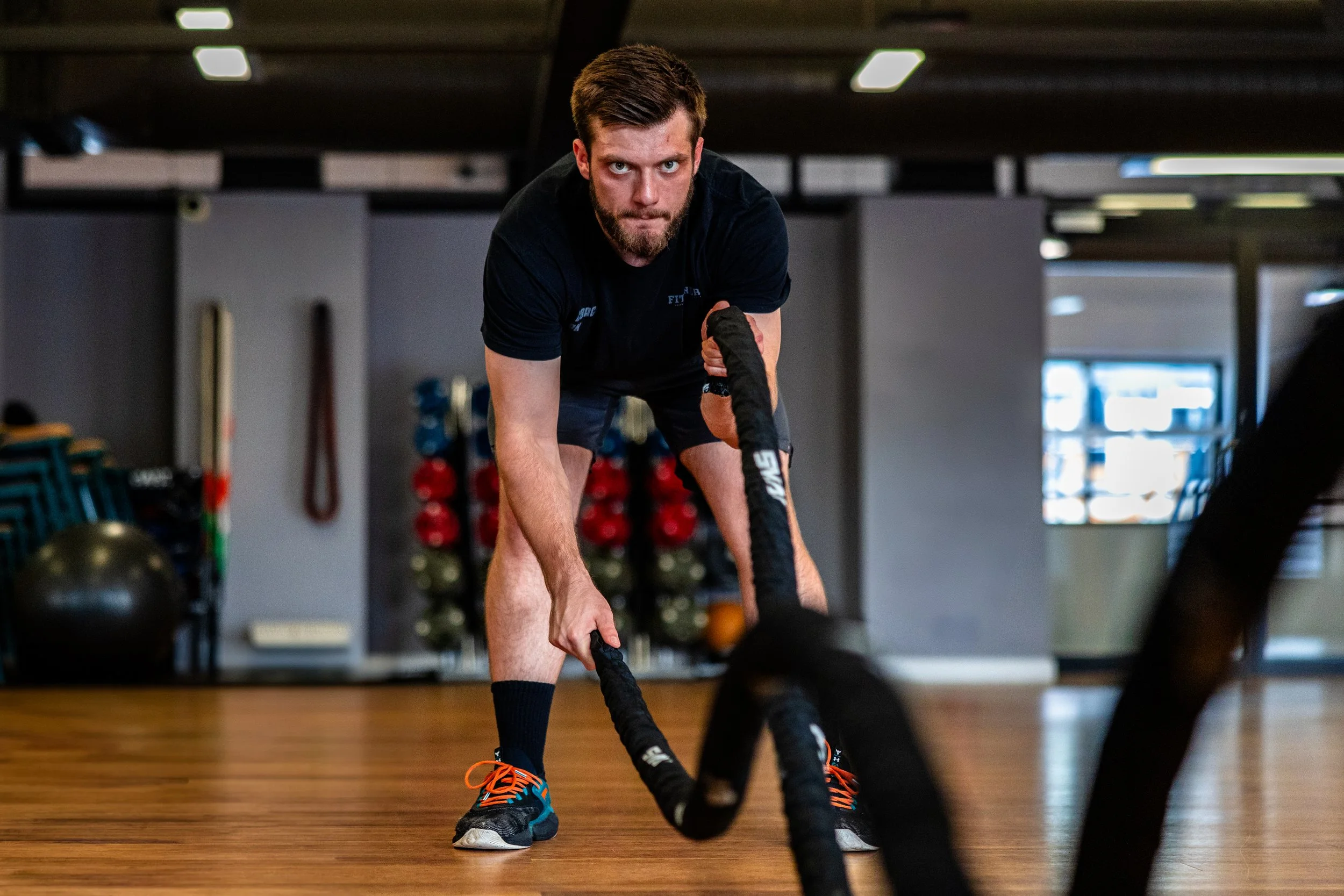 Man with a beard and short hair exercising with battle ropes in a gym.