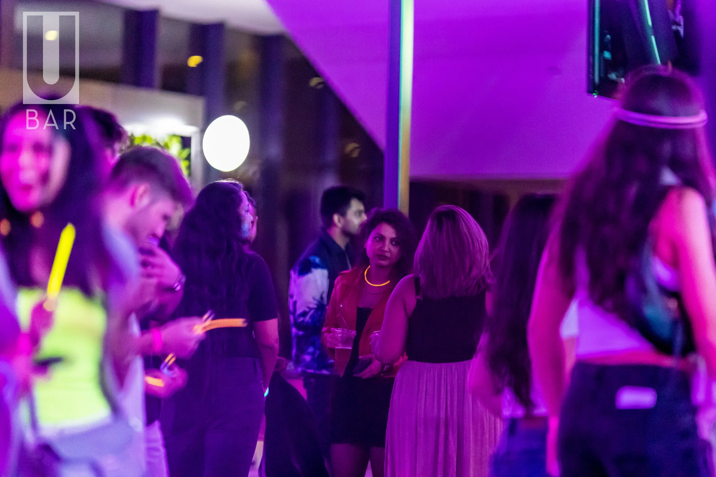 People socializing at a bar or club with colorful lighting.