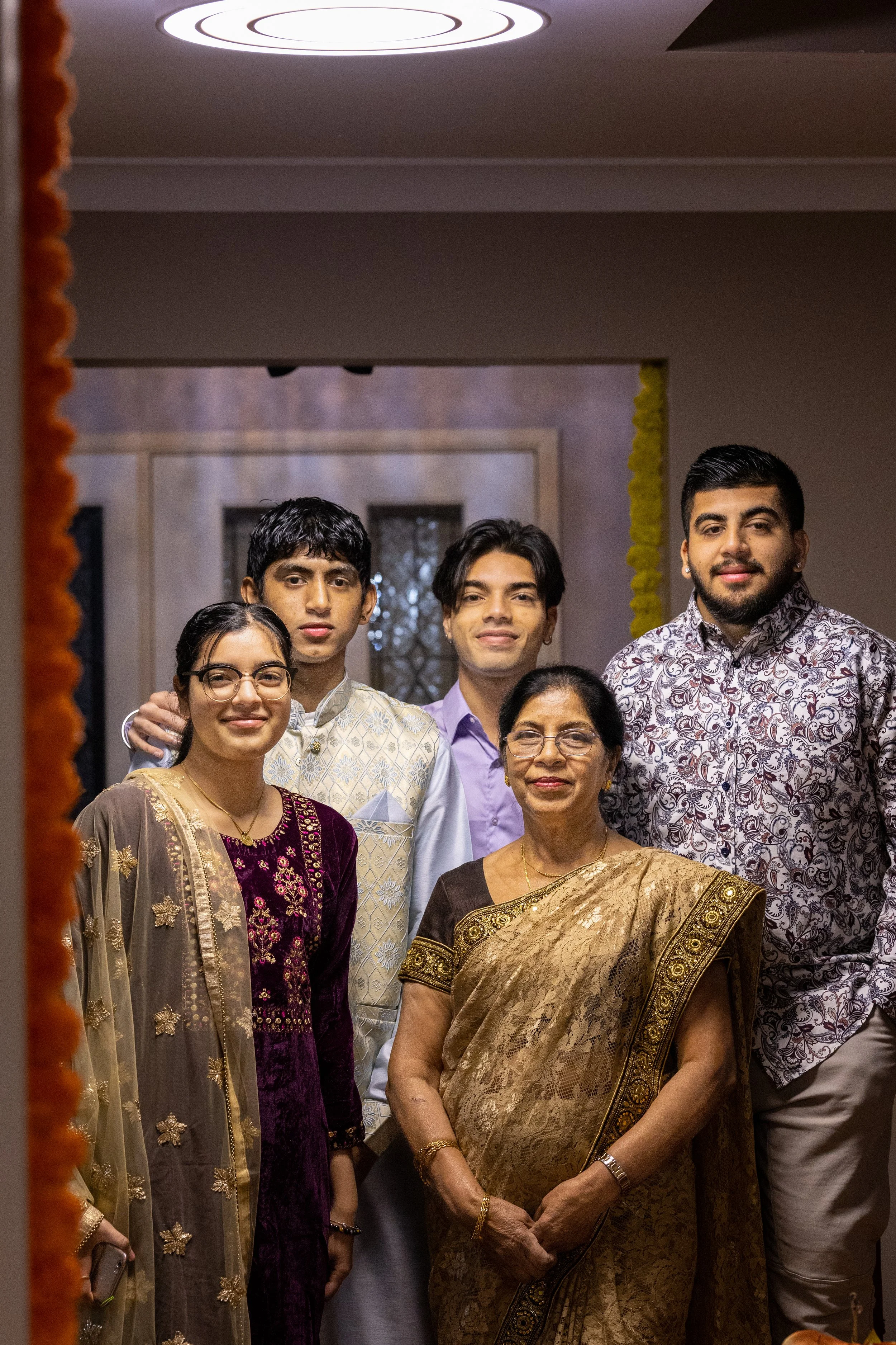 Group of five people celebrating a cultural event, wearing traditional Indian attire, standing together indoors.