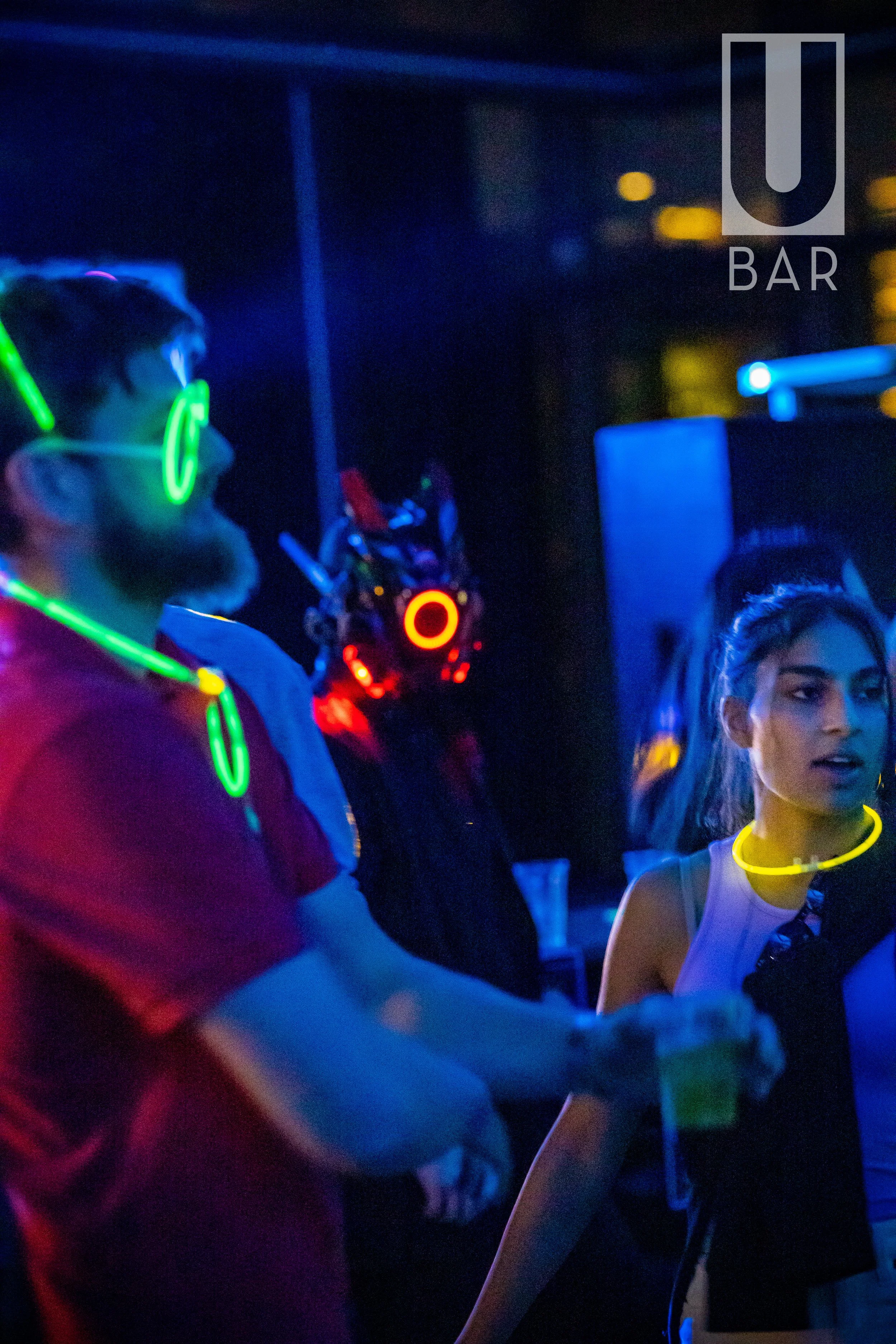 People wearing glow-in-the-dark accessories and headphones at a party or nightclub, with a 