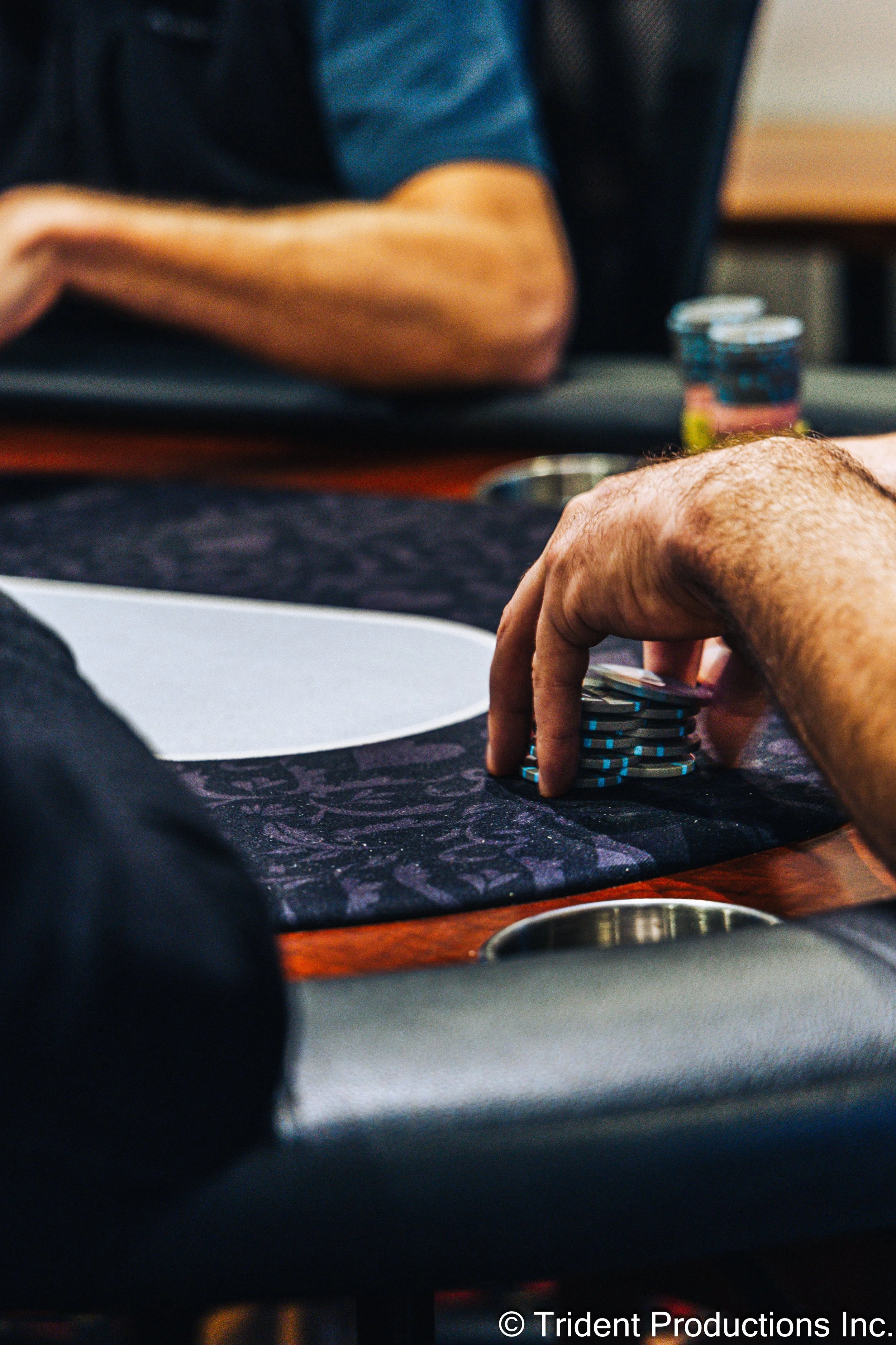 Close-up of a person's hand stacking poker chips on a poker table during a game.