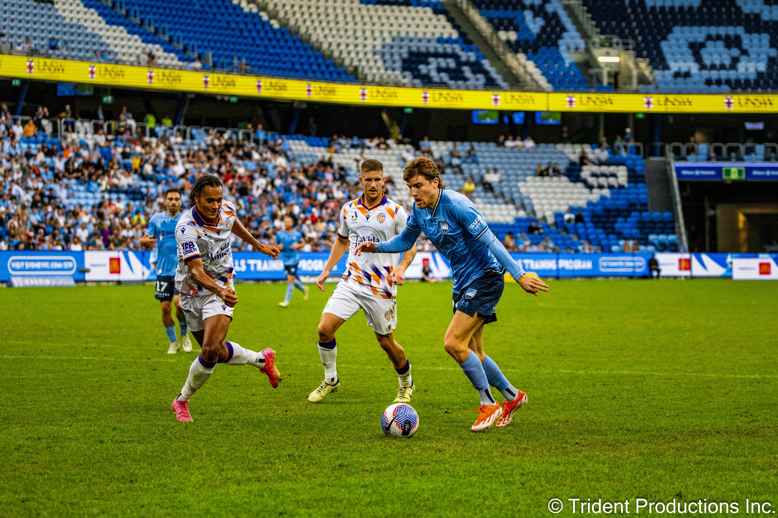 Soccer players competing for ball during a match in a stadium with spectators.
