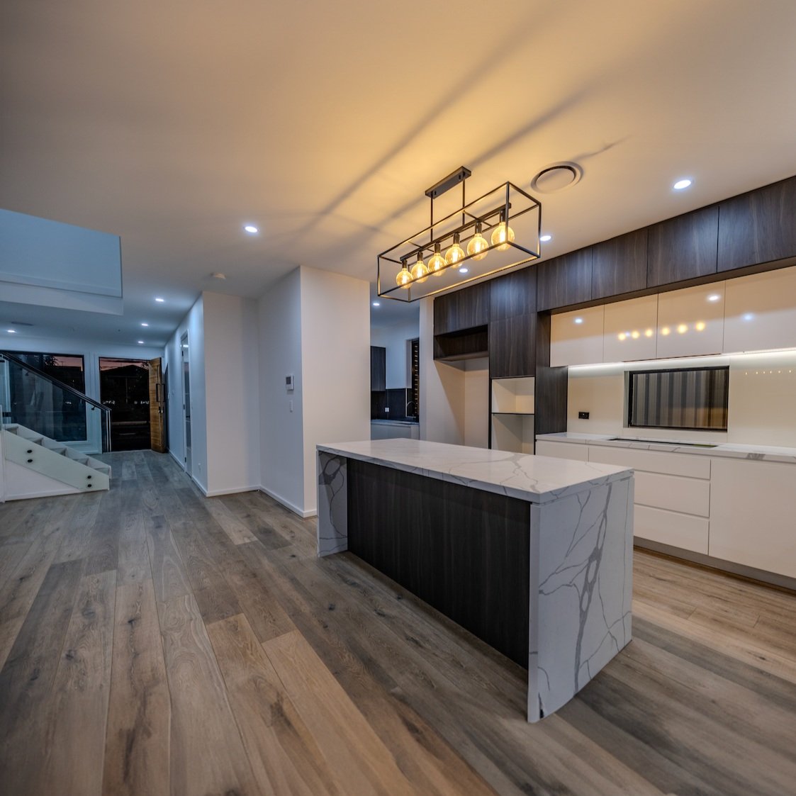 Modern kitchen with a marble island, dark wood cabinetry, and an industrial-style chandelier.