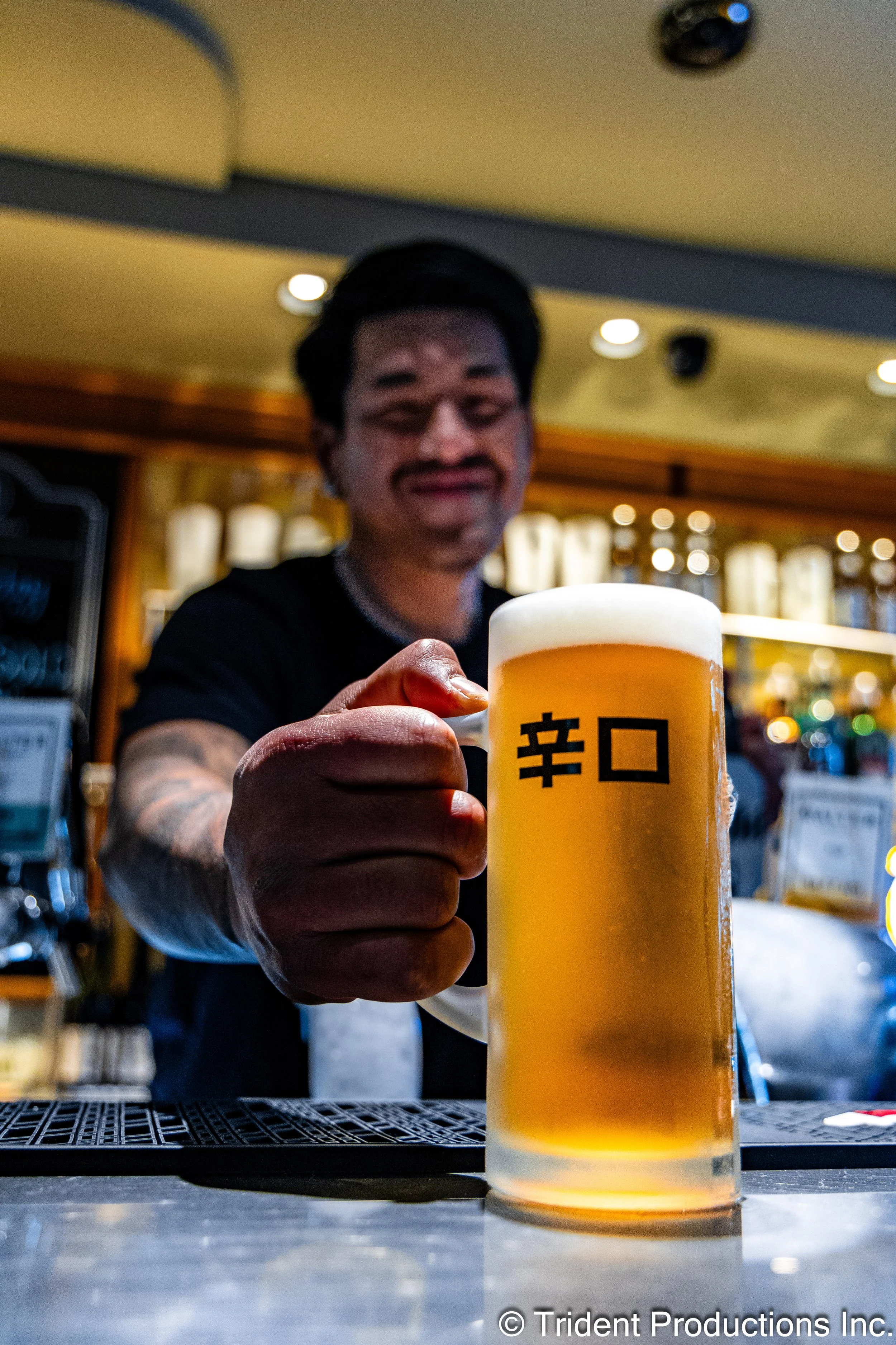 Person holding a large glass of beer with Asian characters on the glass in a bar or restaurant setting.