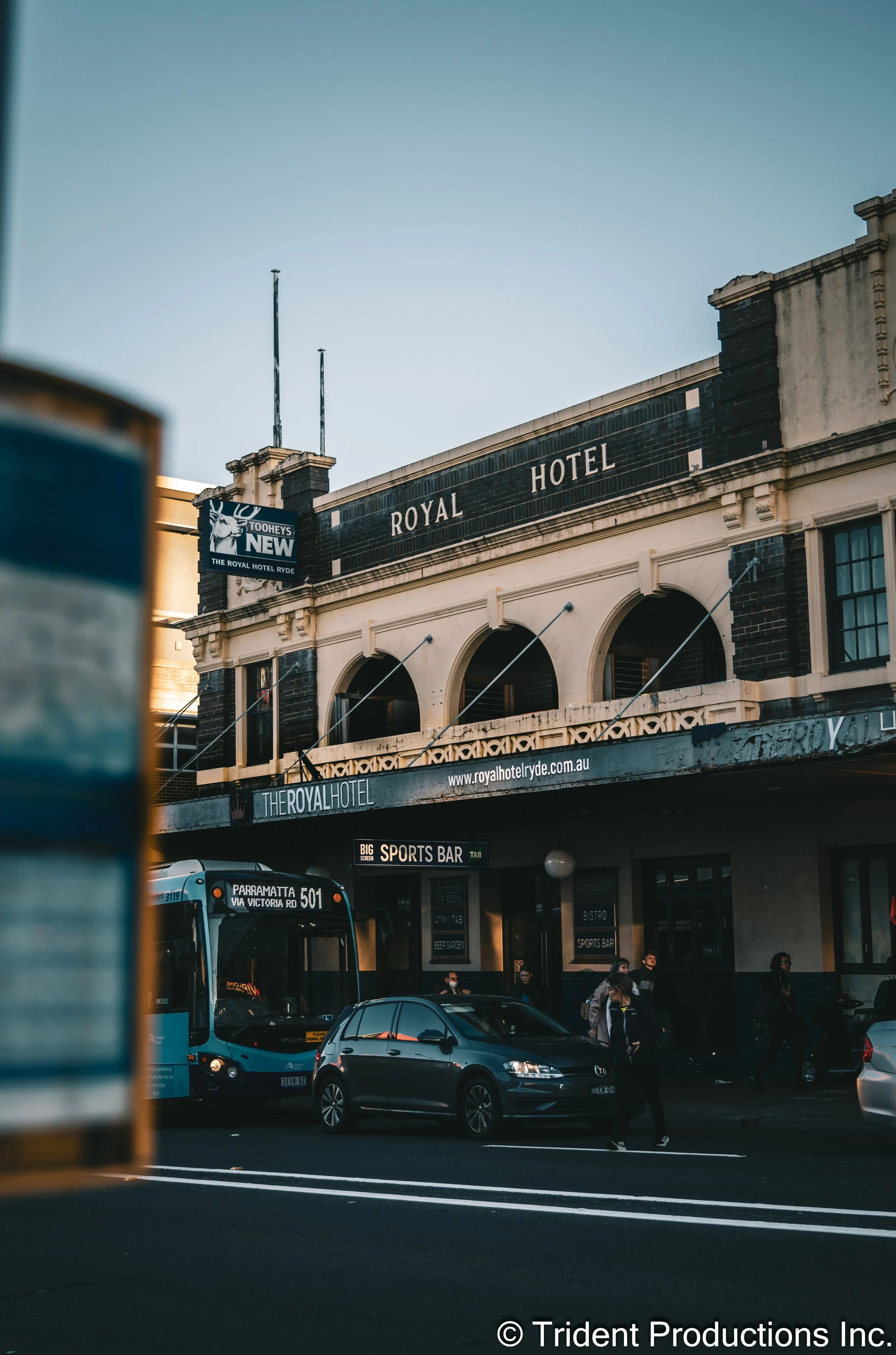 Street view of the Royal Hotel building, with a bus and cars in front, and pedestrians crossing on the road.