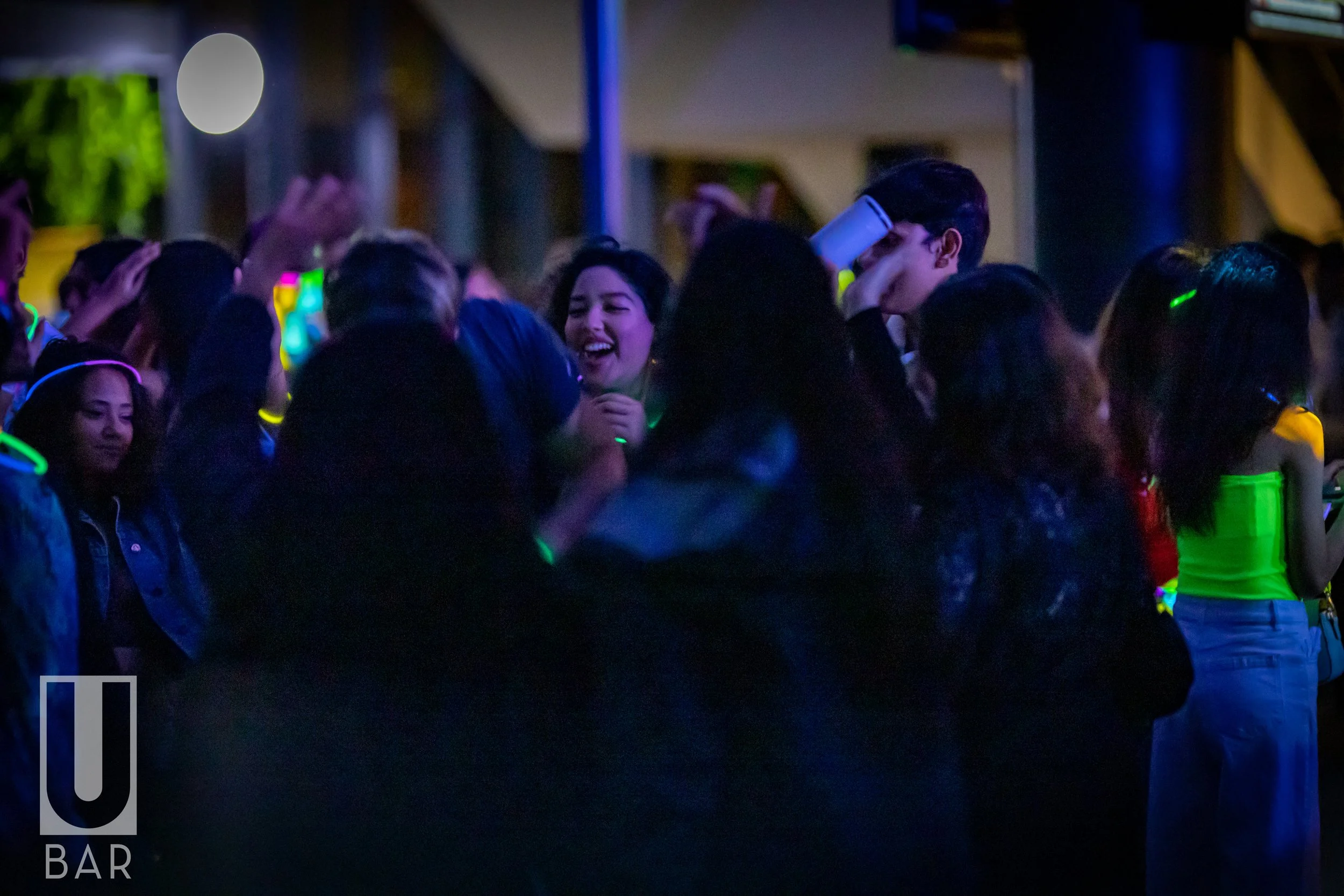 Crowd of young people dancing and enjoying music at a nightclub or party, illuminated by colorful glow sticks and neon lights.