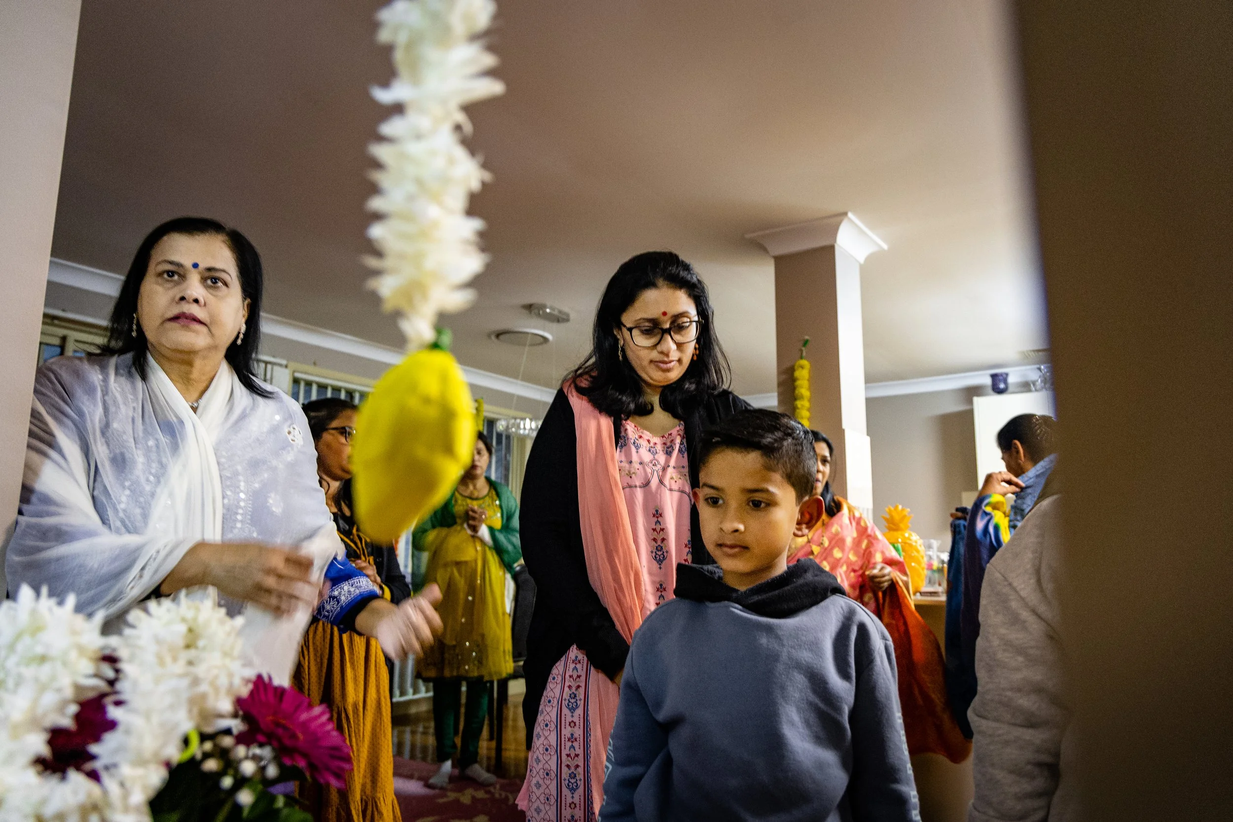 People celebrating a festival indoors, some holding flower garlands, with colorful traditional clothing.