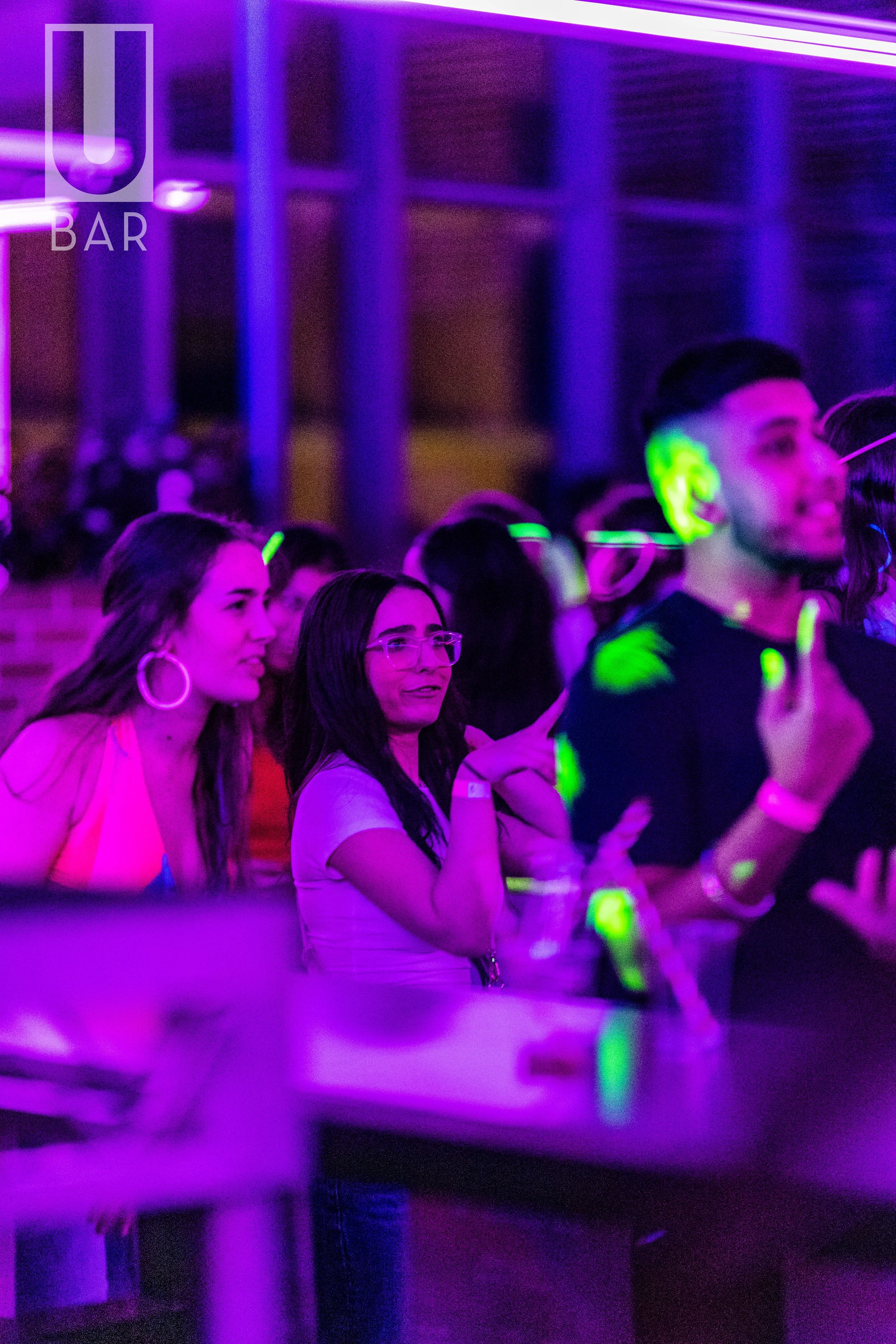 People dancing and enjoying music at a nightclub with purple and green lighting.