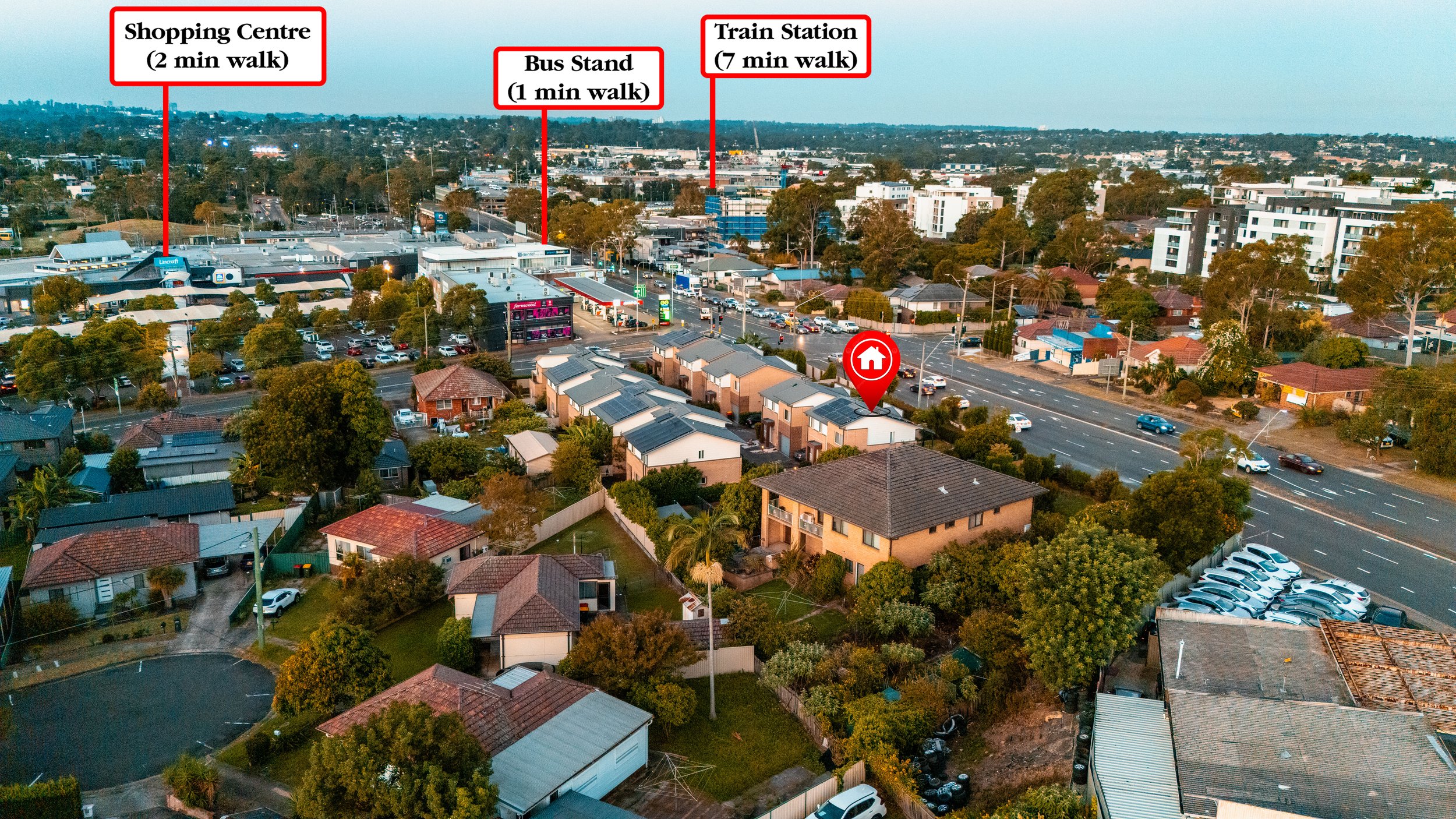 An aerial view of a suburban neighborhood with a main road, residential houses, and commercial buildings. Labels indicate walking distances to nearby amenities: a shopping center 2 minutes away, a bus stand 1 minute away, and a train station 7 minute