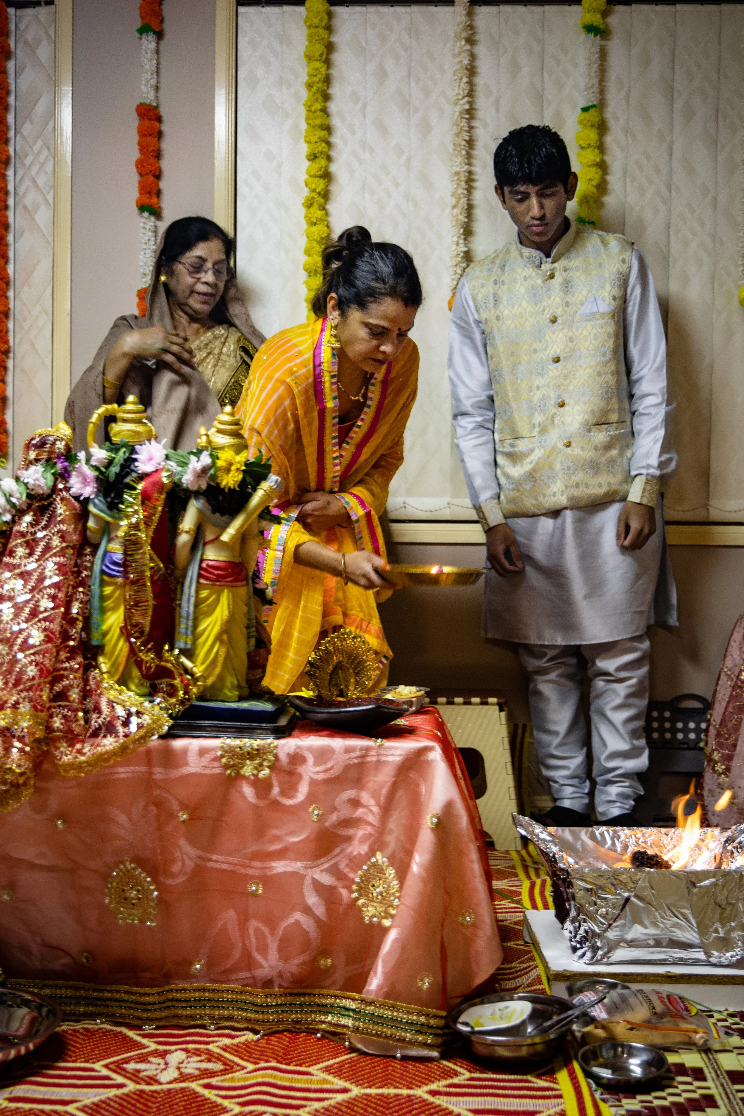People participating in a traditional Hindu religious ceremony with offerings, floral decorations, and fire ritual.