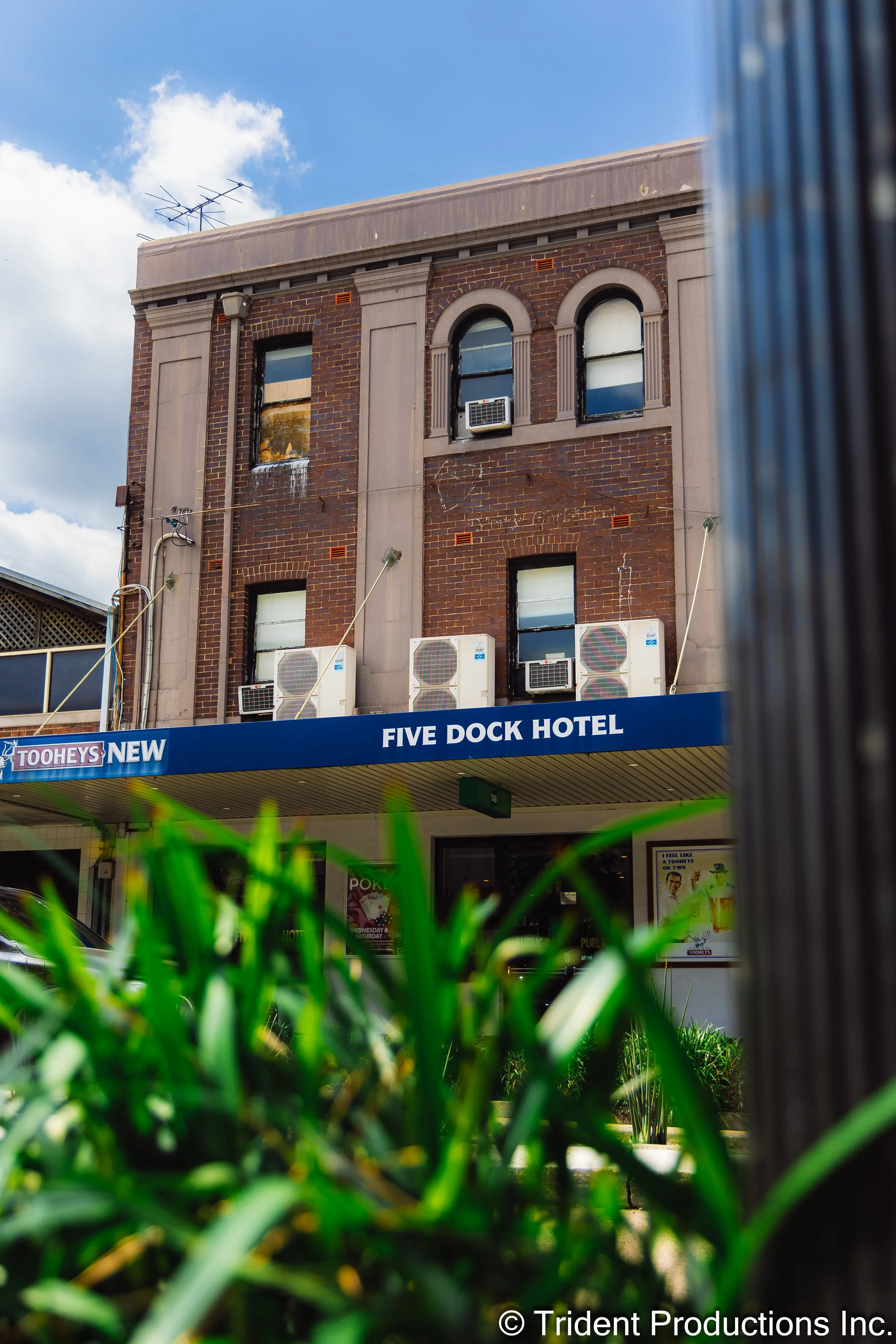 A brick building with a sign that says 'FIVE DOCK HOTEL' in front of a blue sky with clouds.