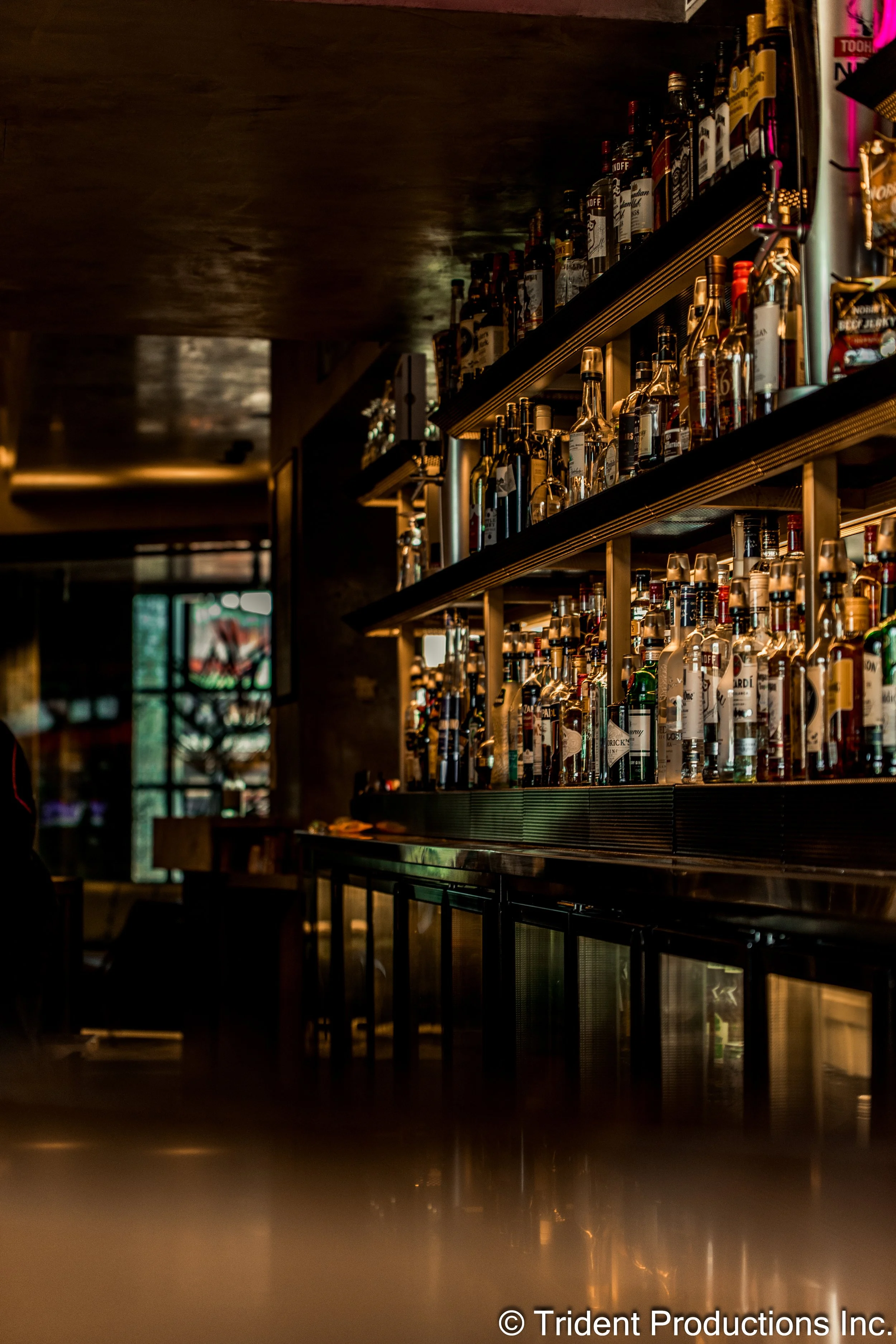 Inside a bar, shelves stocked with various bottles of alcohol, with dim lighting.