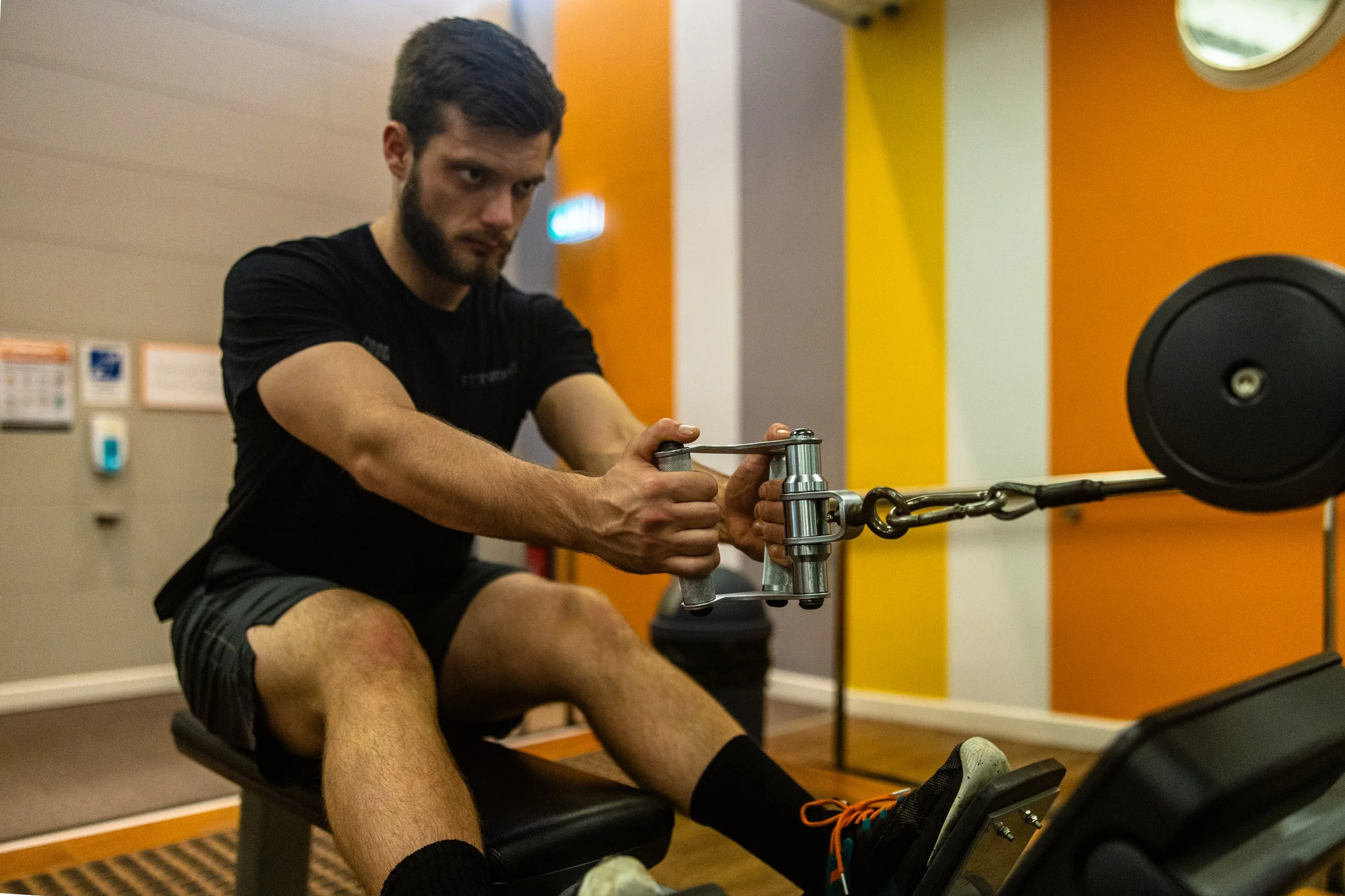 Man exercising on a rowing machine in a gym, pulling the handle with a serious expression.