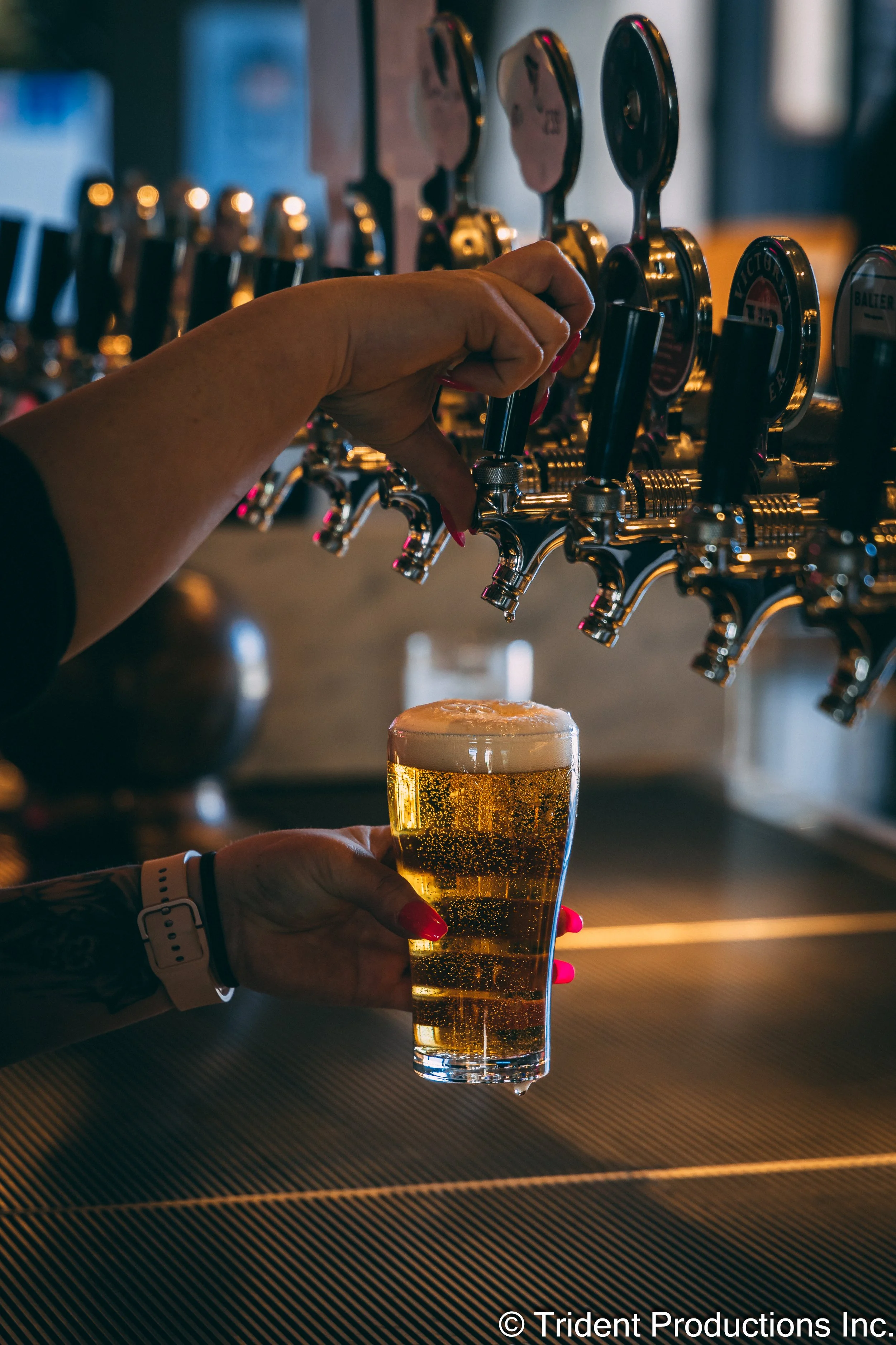 A person pours beer from a tap into a glass at a bar. The bar has multiple beer taps arranged in a row.