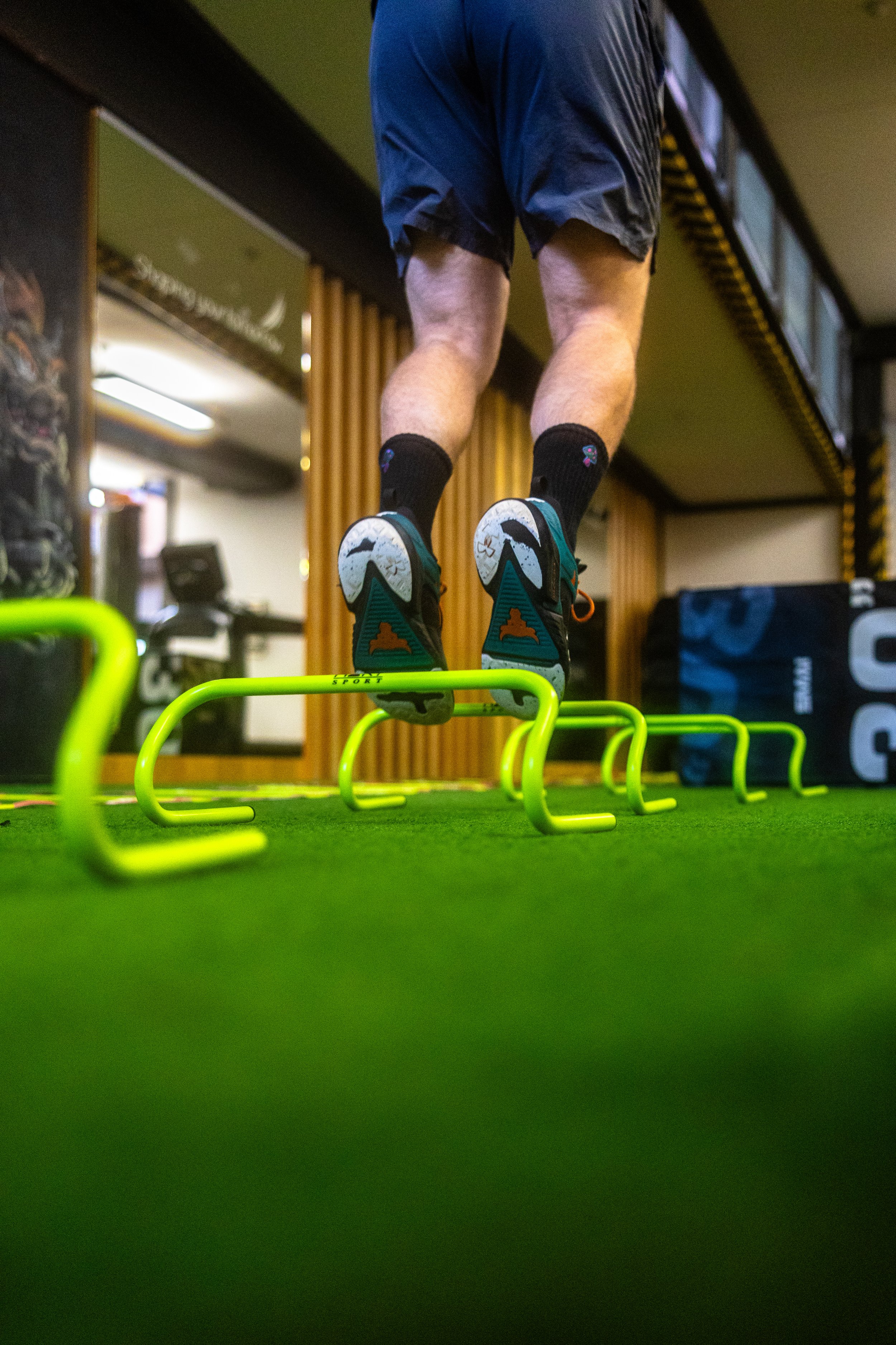 A person jumping over small neon green hurdles on a green gym floor in a fitness gym.