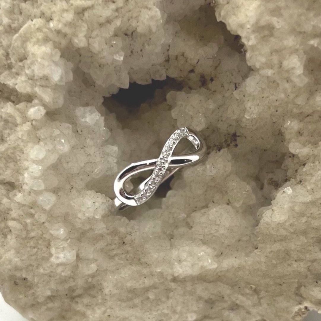 Frequency-infused sterling silver infinity ring with a polished finish, featuring one half adorned with small zirconias, against a crystal background.