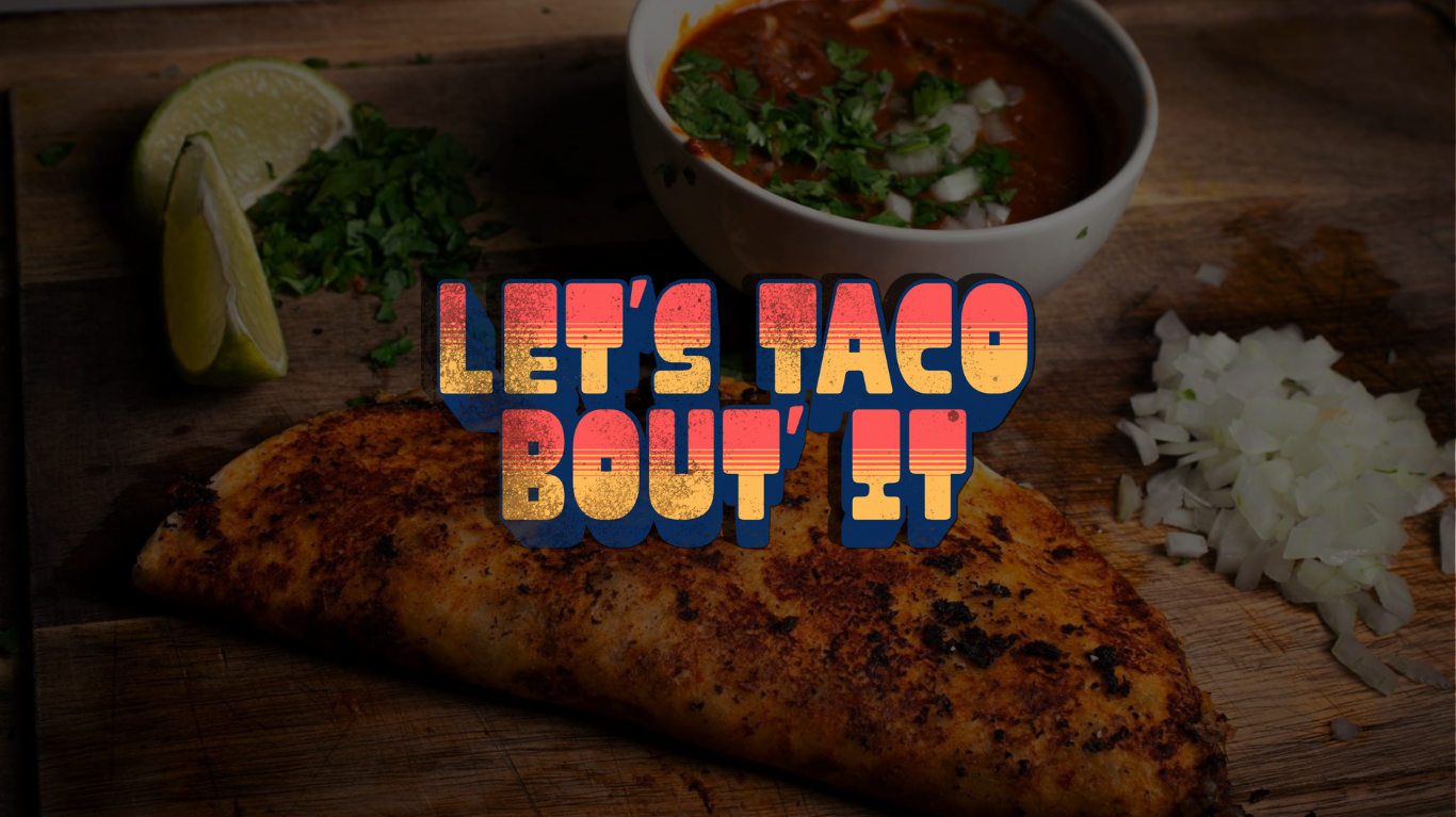 A grilled taco on a wooden surface with chopped onions, lime wedges, cilantro, and a bowl of salsa.