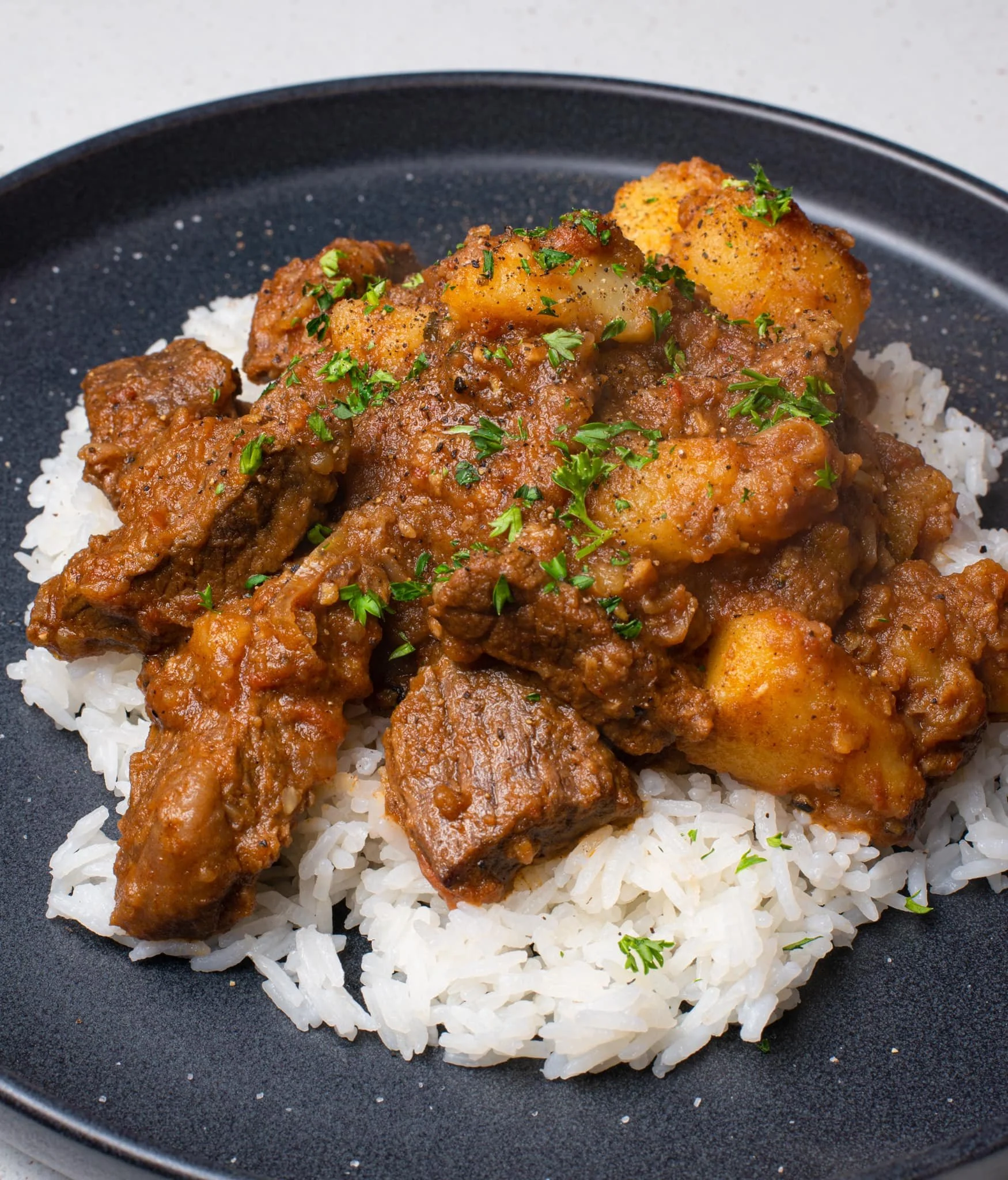 Beef curry served over white rice, garnished with chopped parsley.
