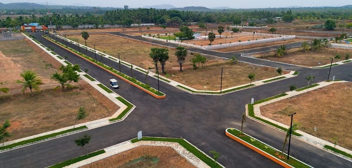 Empty paved roads with street lights and landscaped green strips in a developing residential area, with some trees and an open field.