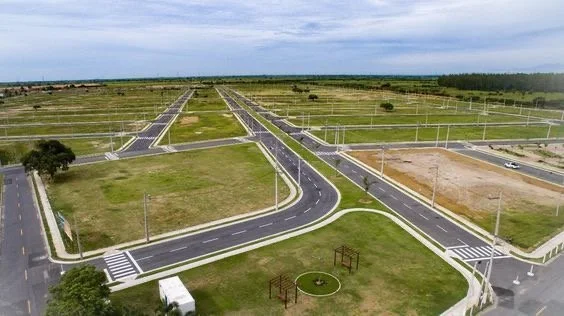 A new, empty residential development with multiple paved roads, streetlights, sidewalks, and small patches of grass and trees, with a cloudy sky overhead.