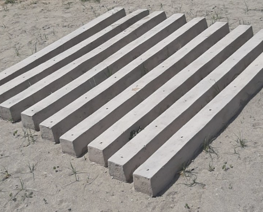 Concrete sandbags stacked in a pyramid shape on sandy ground.