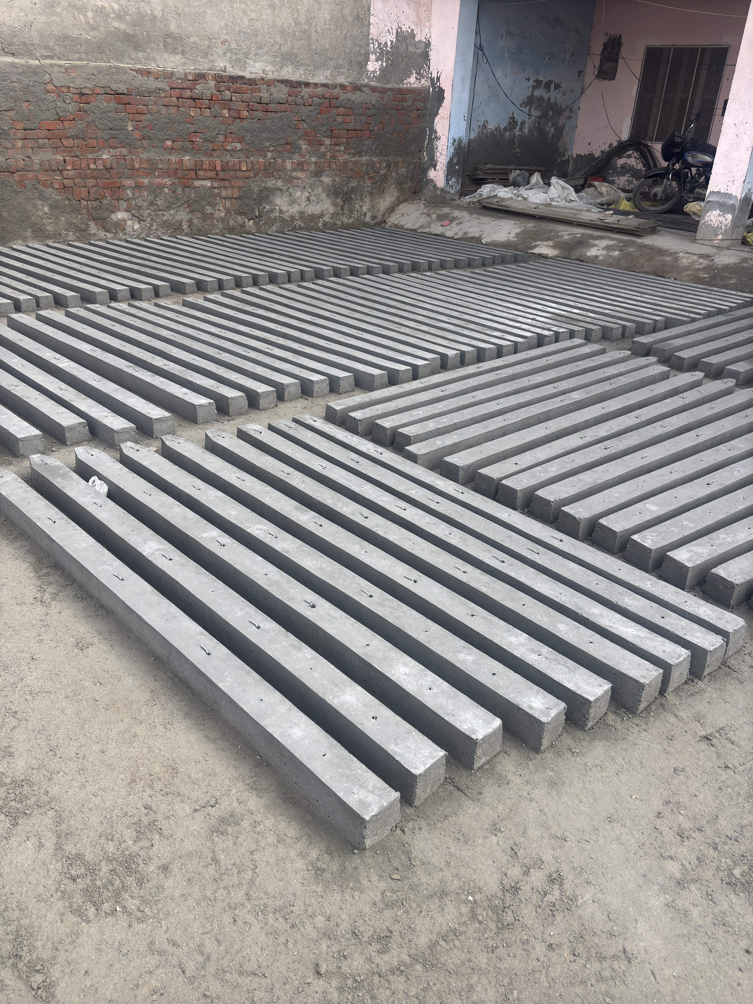 Concrete slabs with parallel ridges arranged on a construction site, with a partially completed brick wall and an old building in the background.