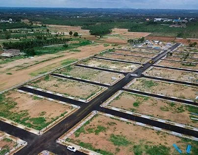 Aerial view of multiple empty, reinforced concrete rectangular fish tanks or ponds in a rural or semi-industrial area, with dirt roads and open fields surrounding them.