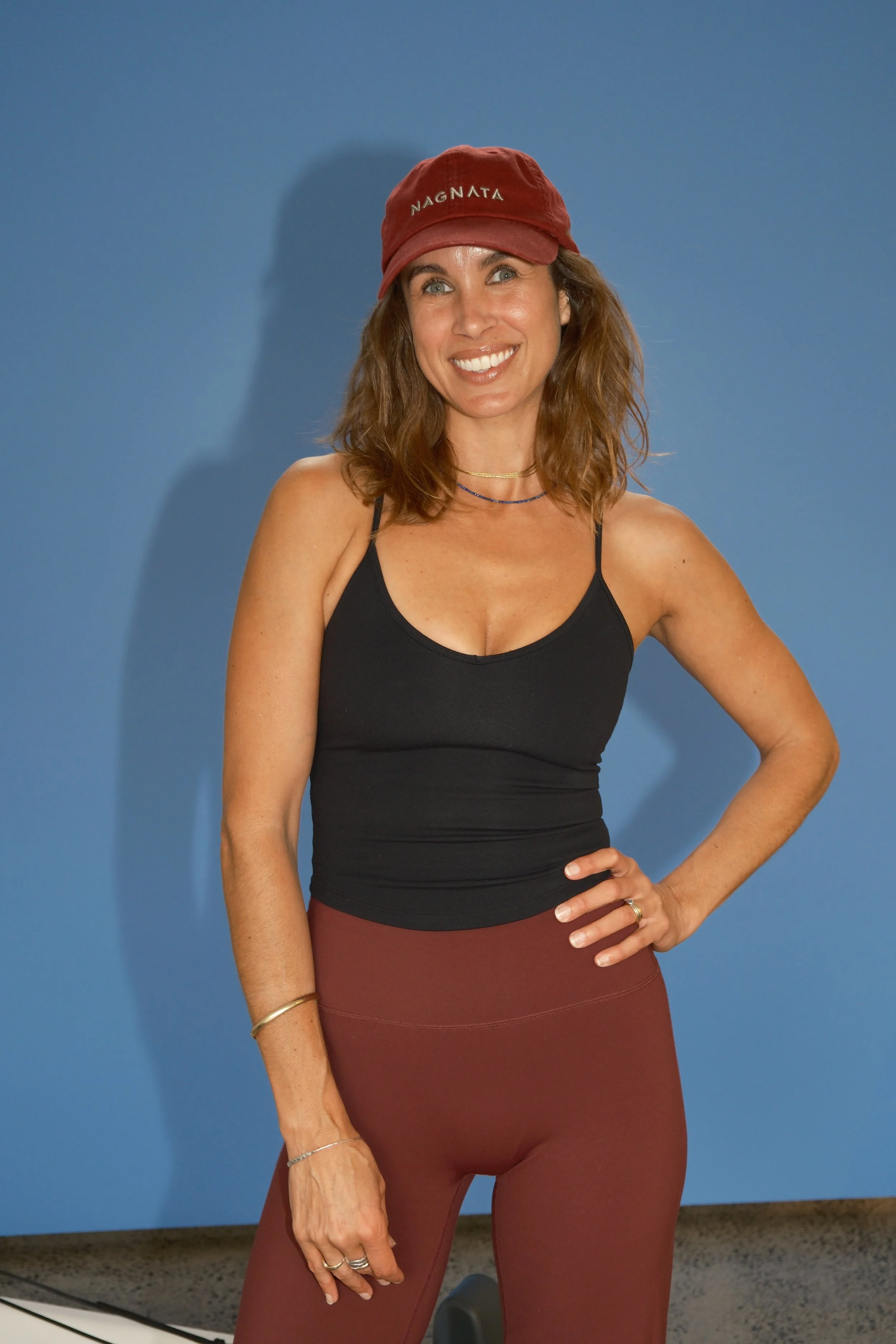A woman with shoulder-length brown hair, sitting at an outdoor table and smiling at the camera.