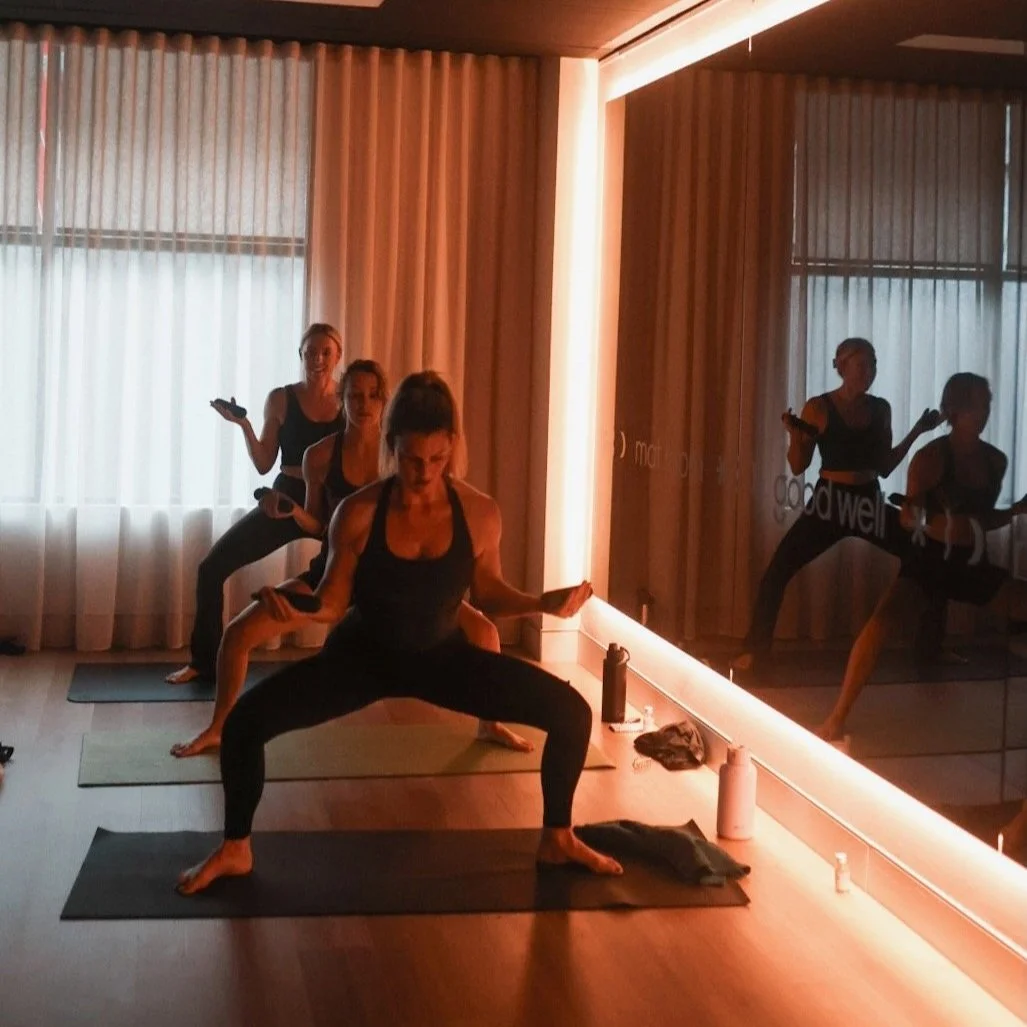 Group of women practicing yoga in a room with soft lighting and large mirrors.