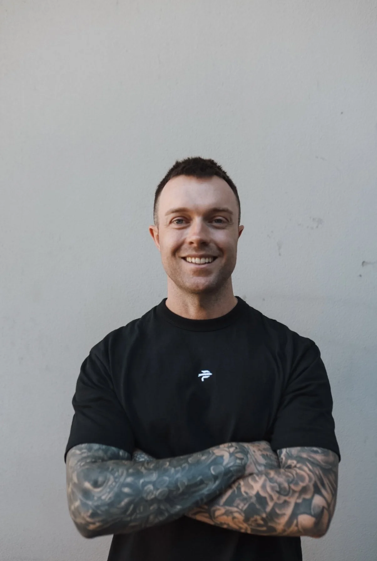 Smiling man with short dark hair and beard, wearing a black t-shirt, standing outdoors at Terrigal.