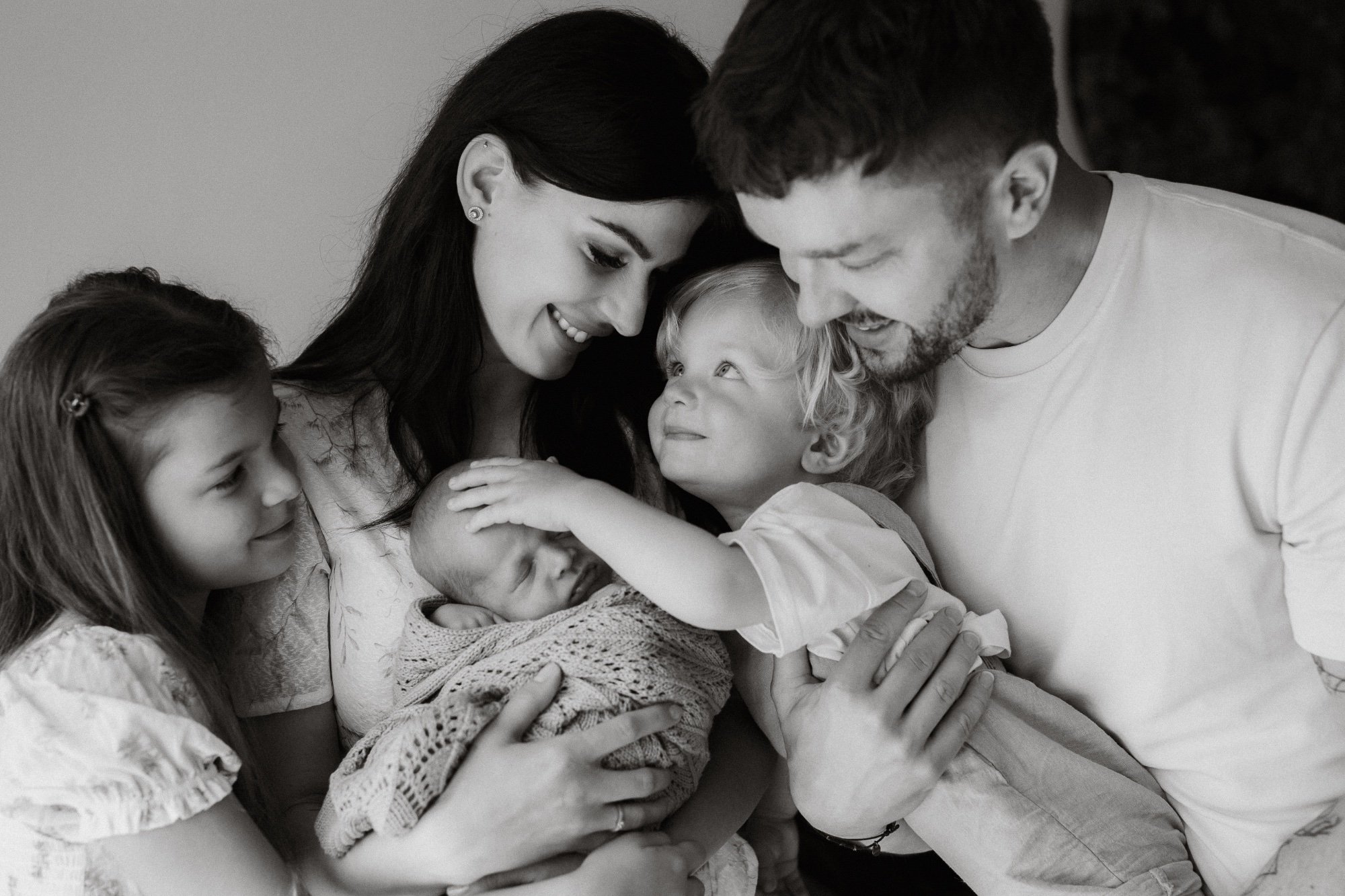 Usmívající se rodina stojí v objetí kolem miminka při newborn focení v Olomouci