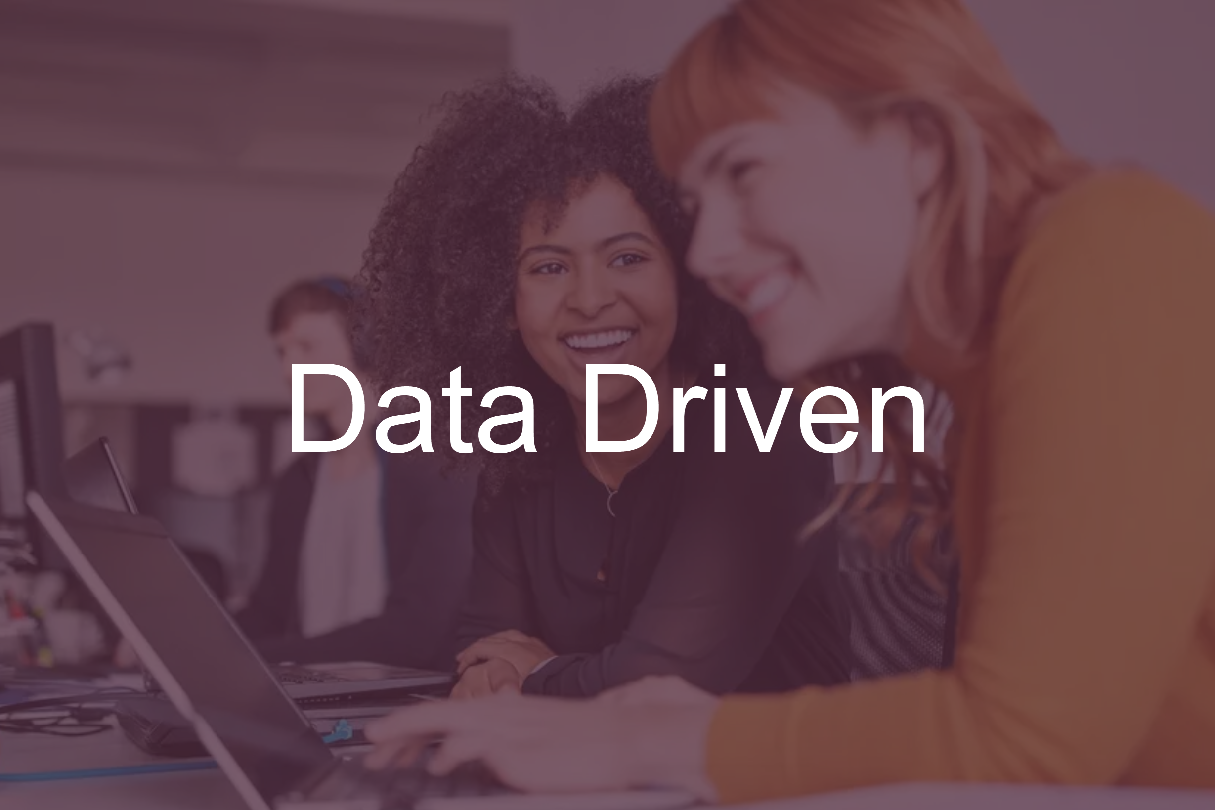 Two women sitting at a desk working on a laptop, smiling and engaged in conversation, with the words "Data Driven" overlaid.